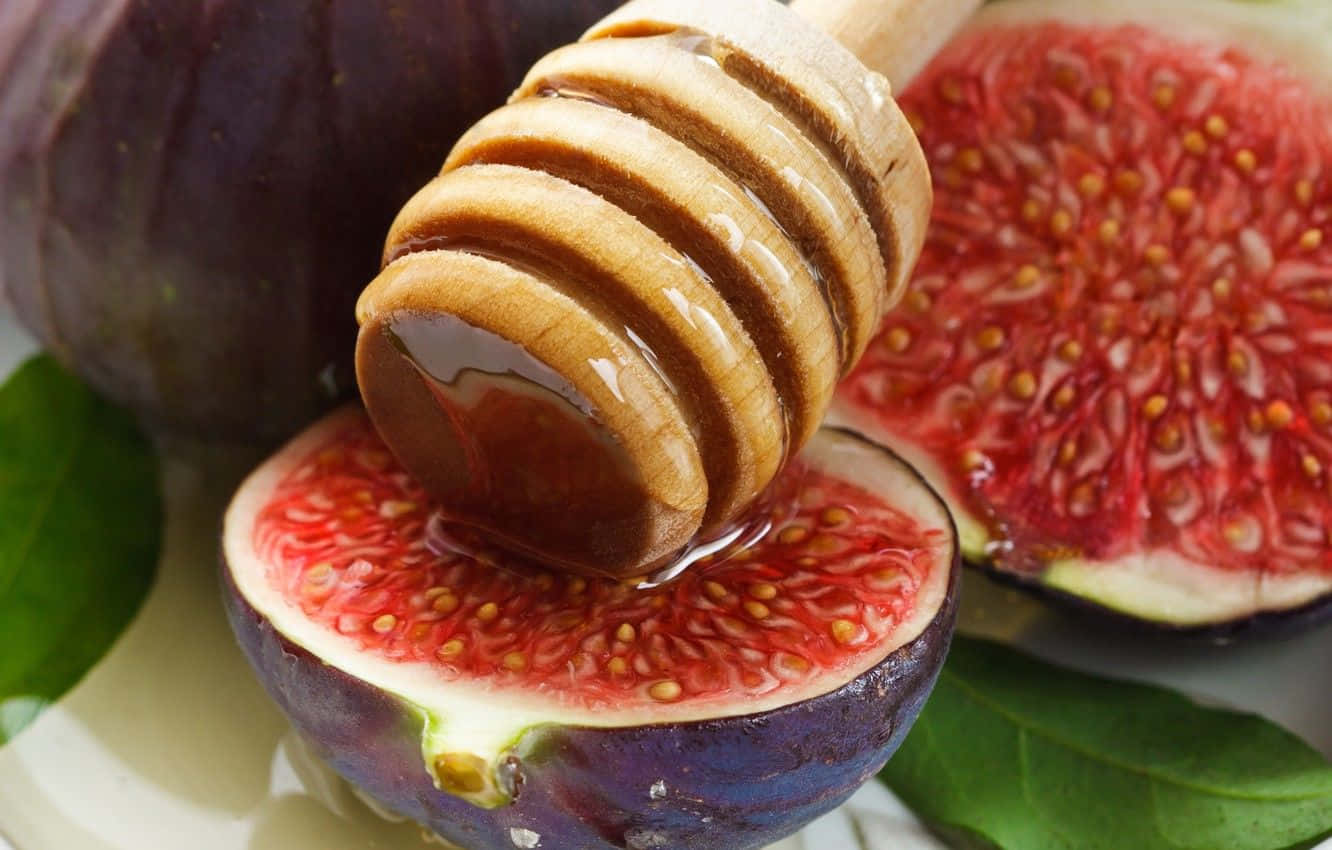 Purple Figs 桌布 壁紙 — 一個木製蜂蜜棒將金黃色的蜂蜜滴到切開的成熟無花果上，露出其粉紅色的果肉和種子。