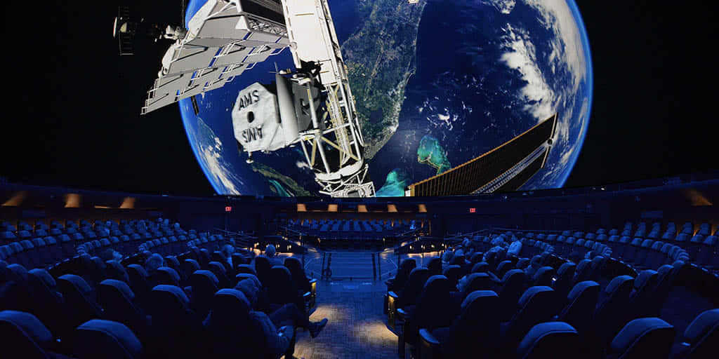Planetarium 桌布 壁紙 — 一個未來風格的劇院，座位排列面向一個巨大的穹頂屏幕，顯示衛星在夜間繞地球運行。