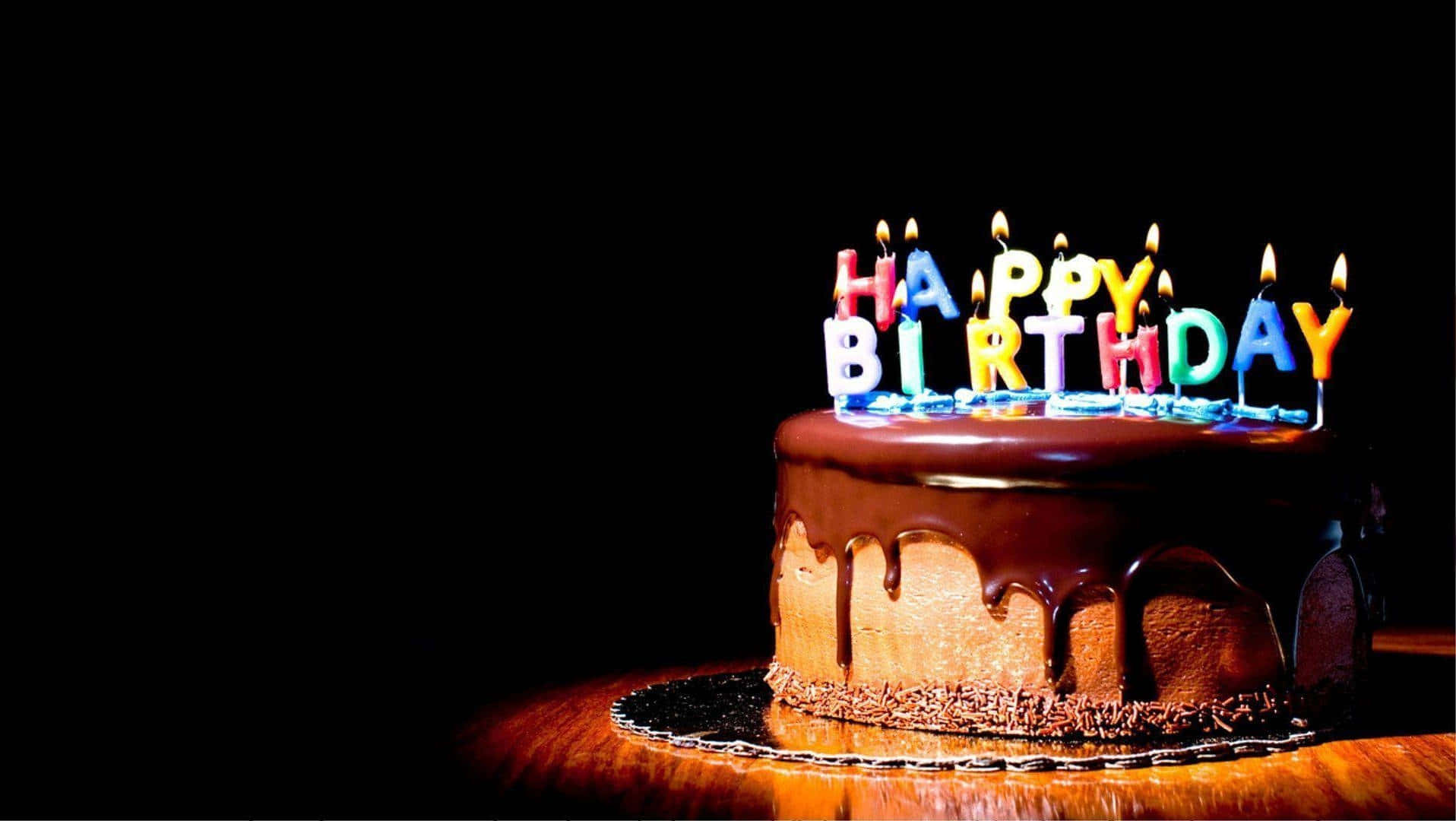 生日蛋糕 桌布 壁紙 — 一個朱古力滴落蛋糕，上面有色彩繽紛的「HAPPY BIRTHDAY」蠟燭在黑色背景前發光。