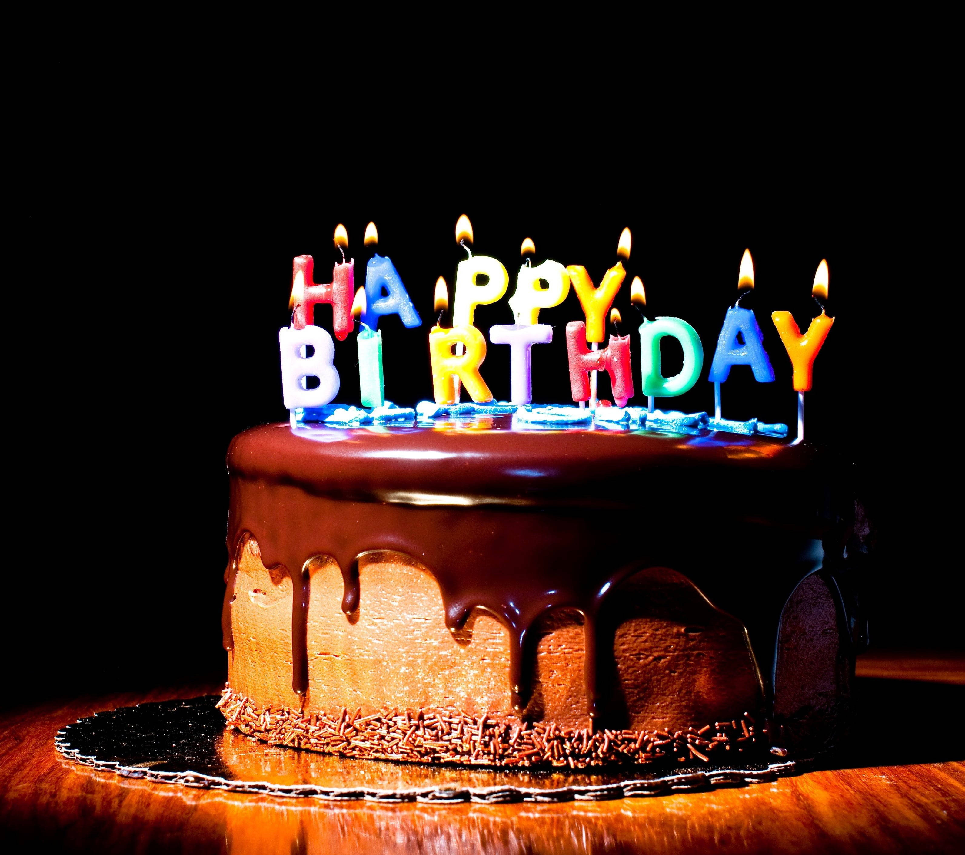 Birthday 桌布 壁紙 — 一個朱古力生日蛋糕，上面有滴落的糖霜和色彩繽紛的點燃蠟燭，在黑色背景上拼出生日快樂。
