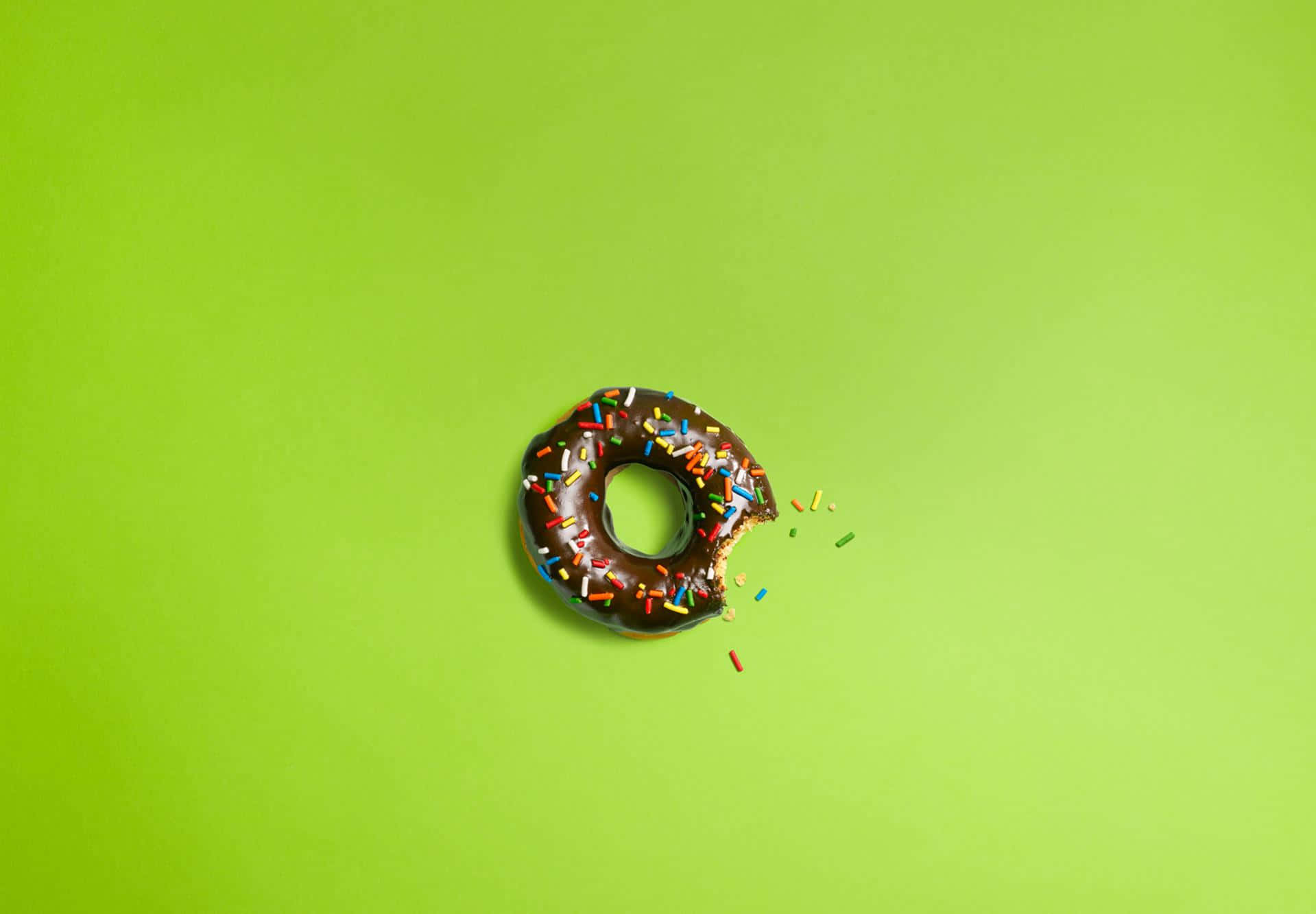 donuts 桌布 壁紙 — 一個朱古力糖霜冬甩，上面有彩色糖針，放在鮮綠色背景上，被咬了一口。