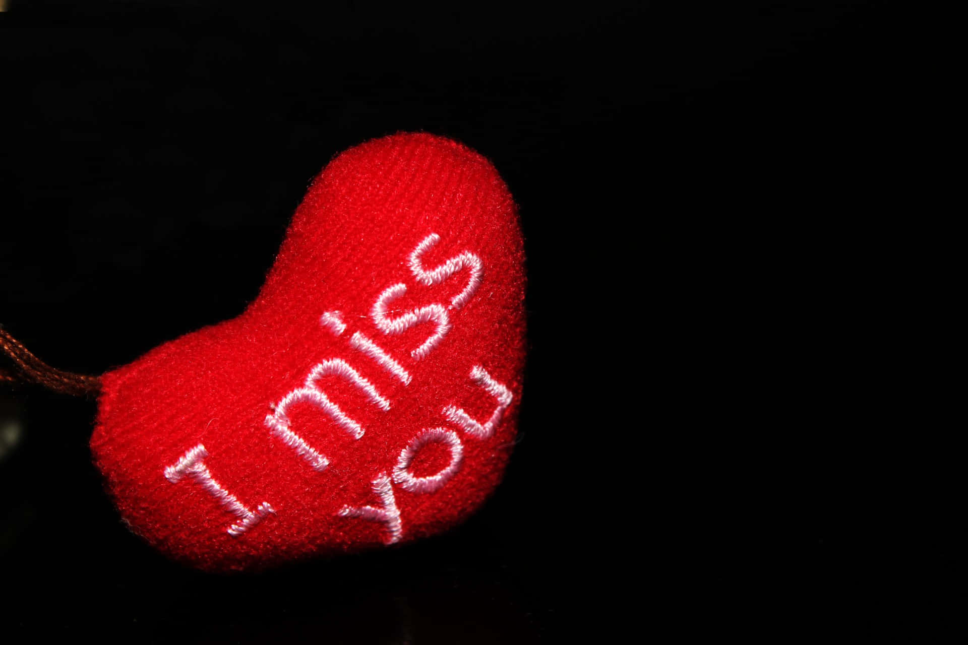 I Miss You 桌布 壁紙 — 一個柔軟的紅色編織心形，帶有白色刺繡文字「我想你」，在漆黑的背景上閃耀。