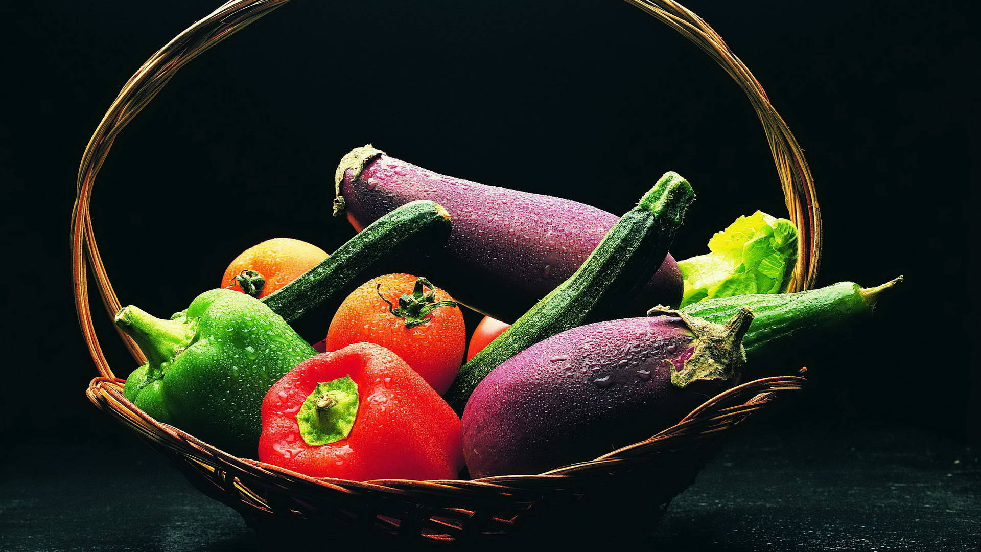 Vegetable 桌布 壁紙 — 一個柳條籃子裝滿了色彩鮮豔的新鮮蔬菜，如茄子、翠玉瓜、番茄和燈籠椒，在深色背景下閃爍著水珠。