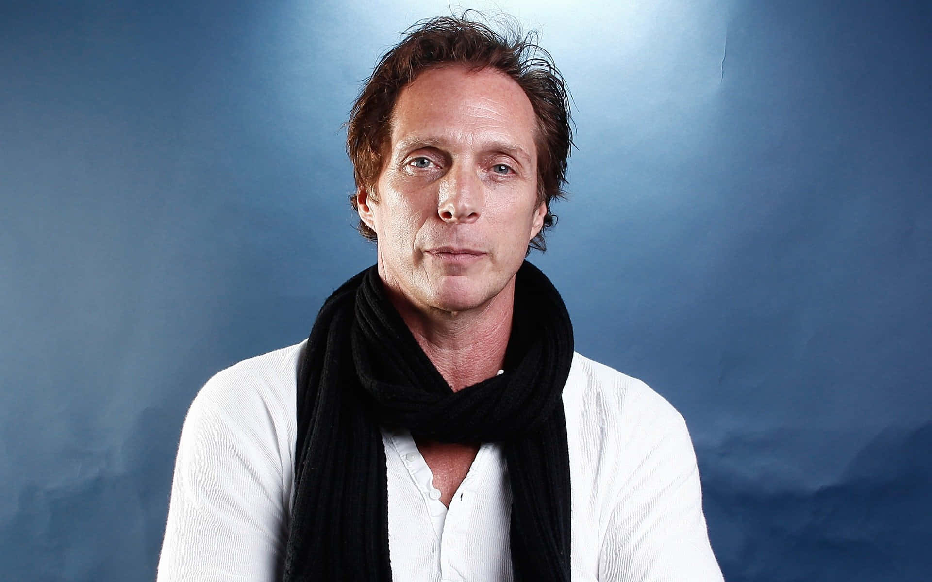 William Fichtner 桌布 壁紙 — 一個棕色亂髮的男人，在帶紋理的藍色攝影棚背景前，戴著黑色圍巾，穿著白色襯衫。