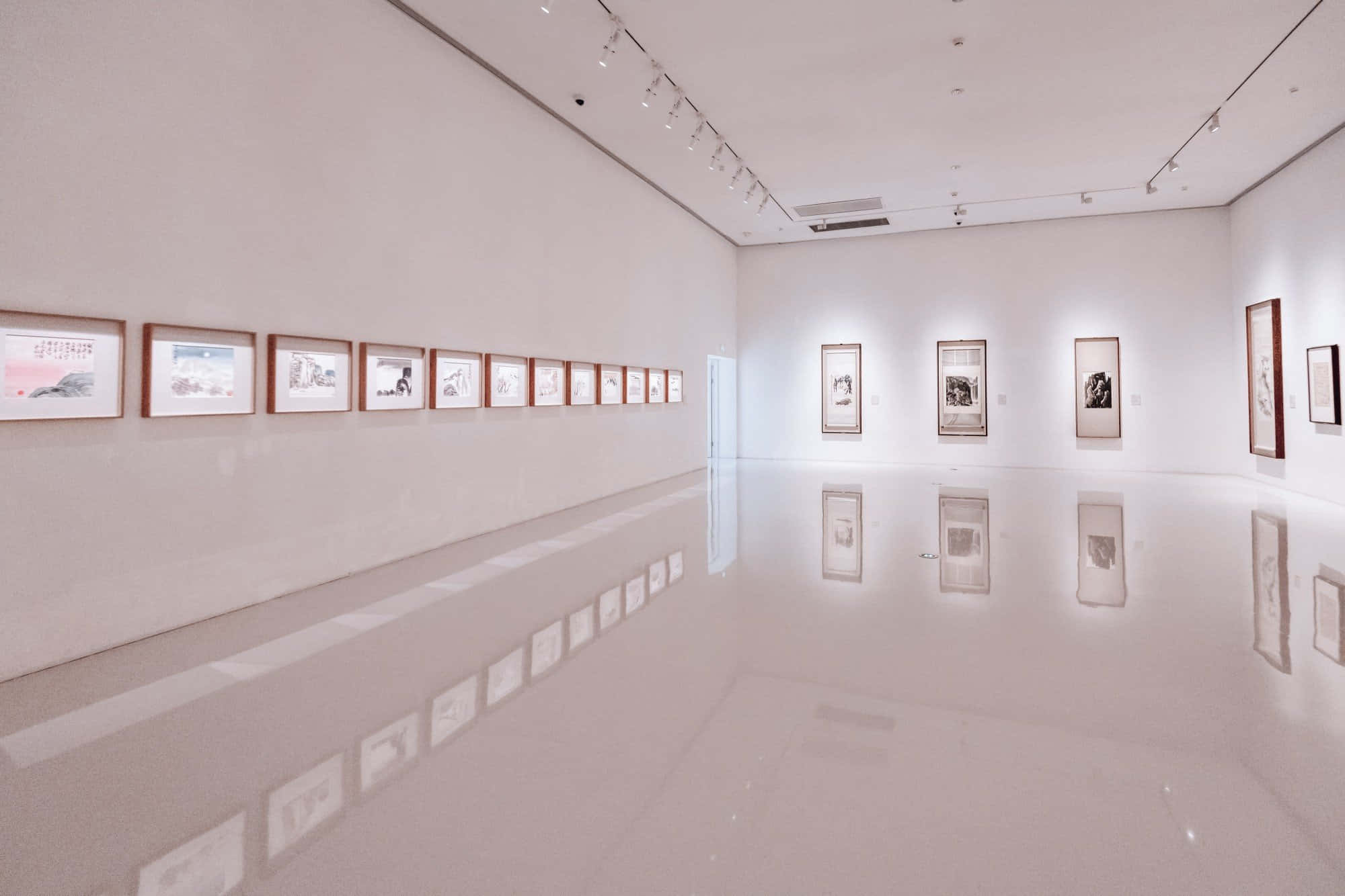 Museum 桌布 壁紙 — 一個極簡主義藝術畫廊，白色牆壁上排列著裱框藝術品，在明亮聚光燈下映照在光澤地板上。