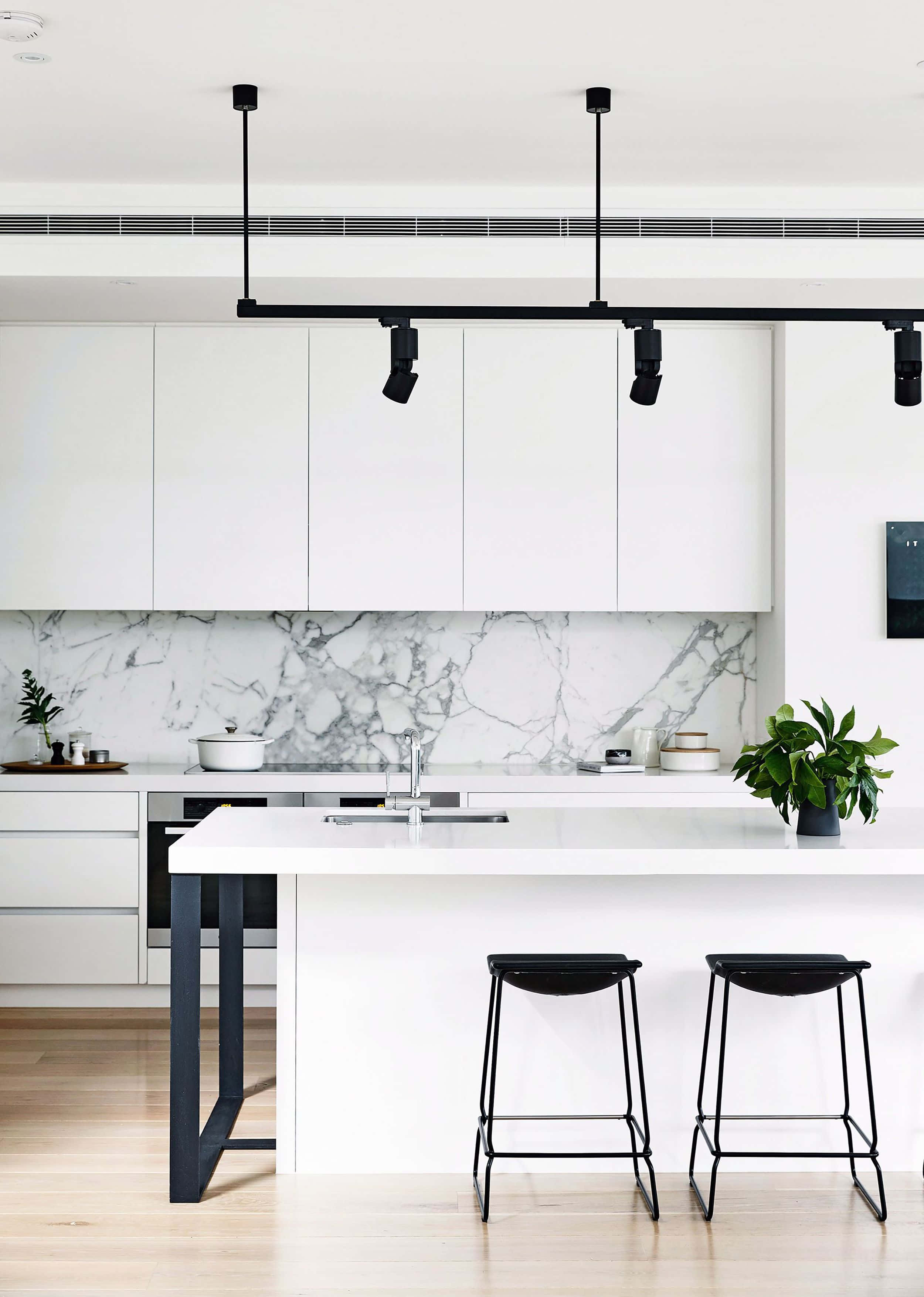 Minimalist Design 桌布 壁紙 — 一個極簡現代廚房，配有白色櫥櫃、大理石防濺板和黑色吧檯凳，下方是時尚的軌道照明。