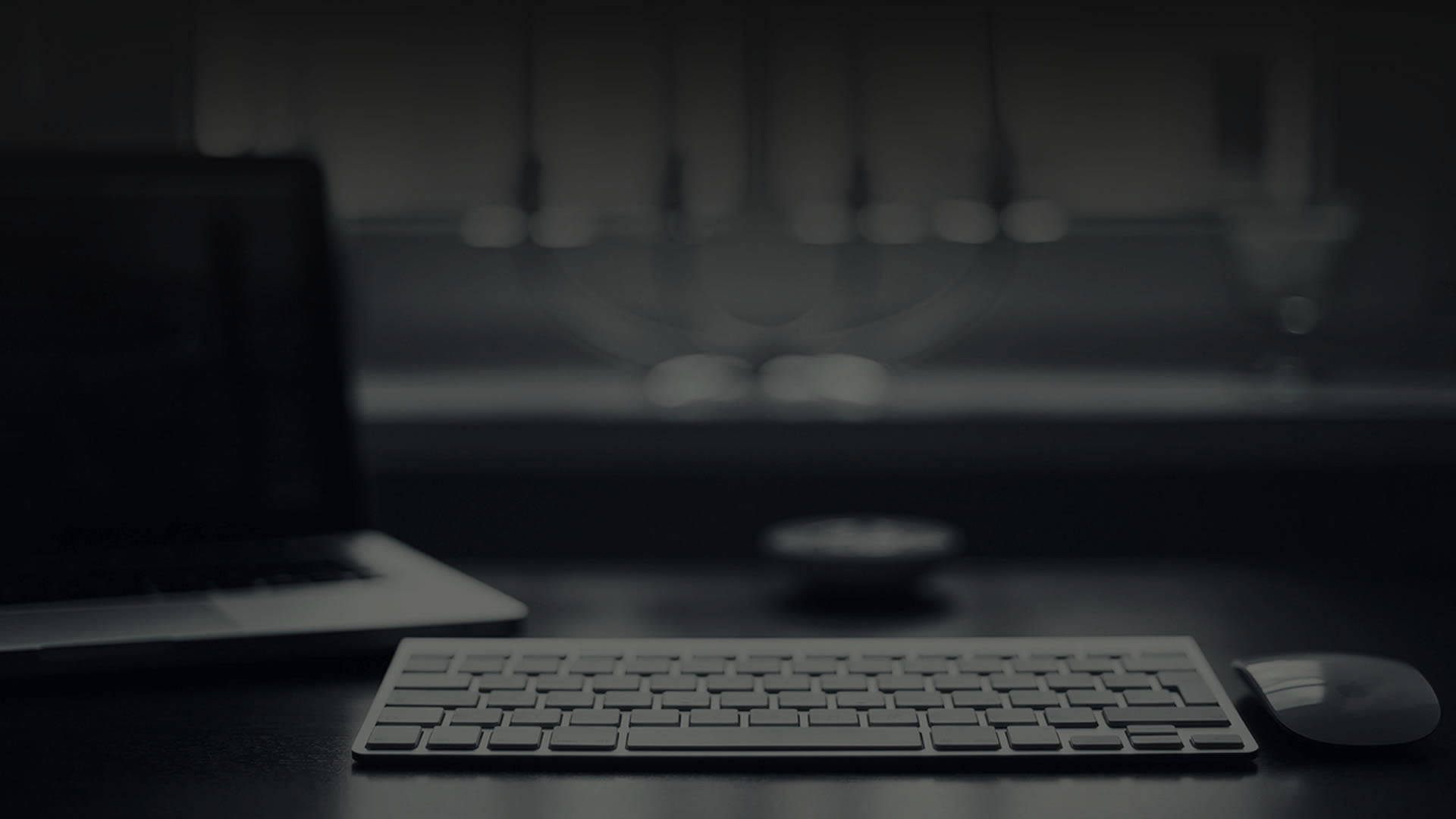 Laptop 桌布 壁紙 — 一個極簡的深灰色工作空間，桌上有鍵盤、滑鼠和手提電腦，背景有模糊的眼鏡。