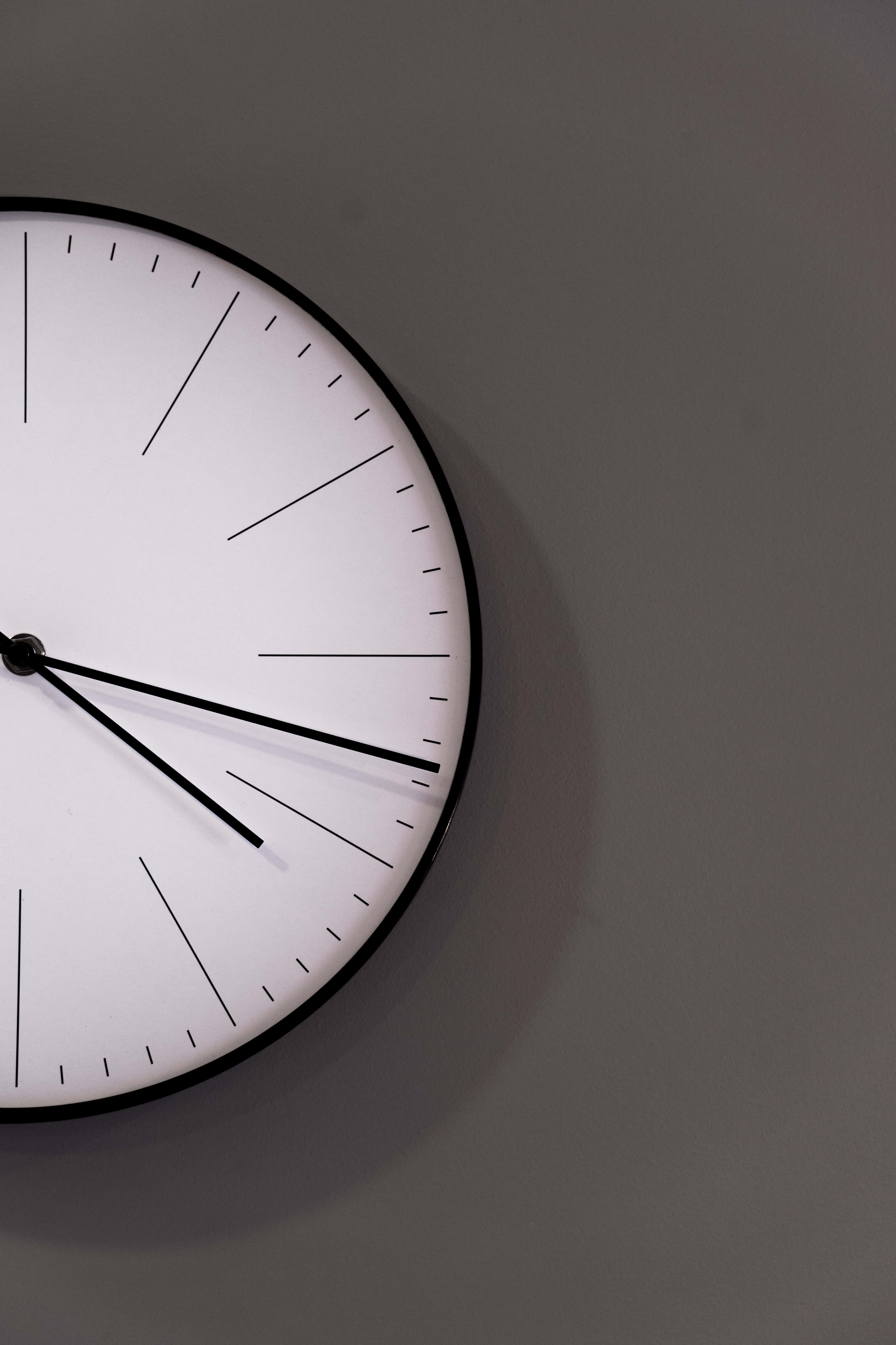 Clocks 桌布 壁紙 — 一個極簡的黑白掛牆鐘，配有幼細指針和幾何標記，掛在柔和的灰色牆上。