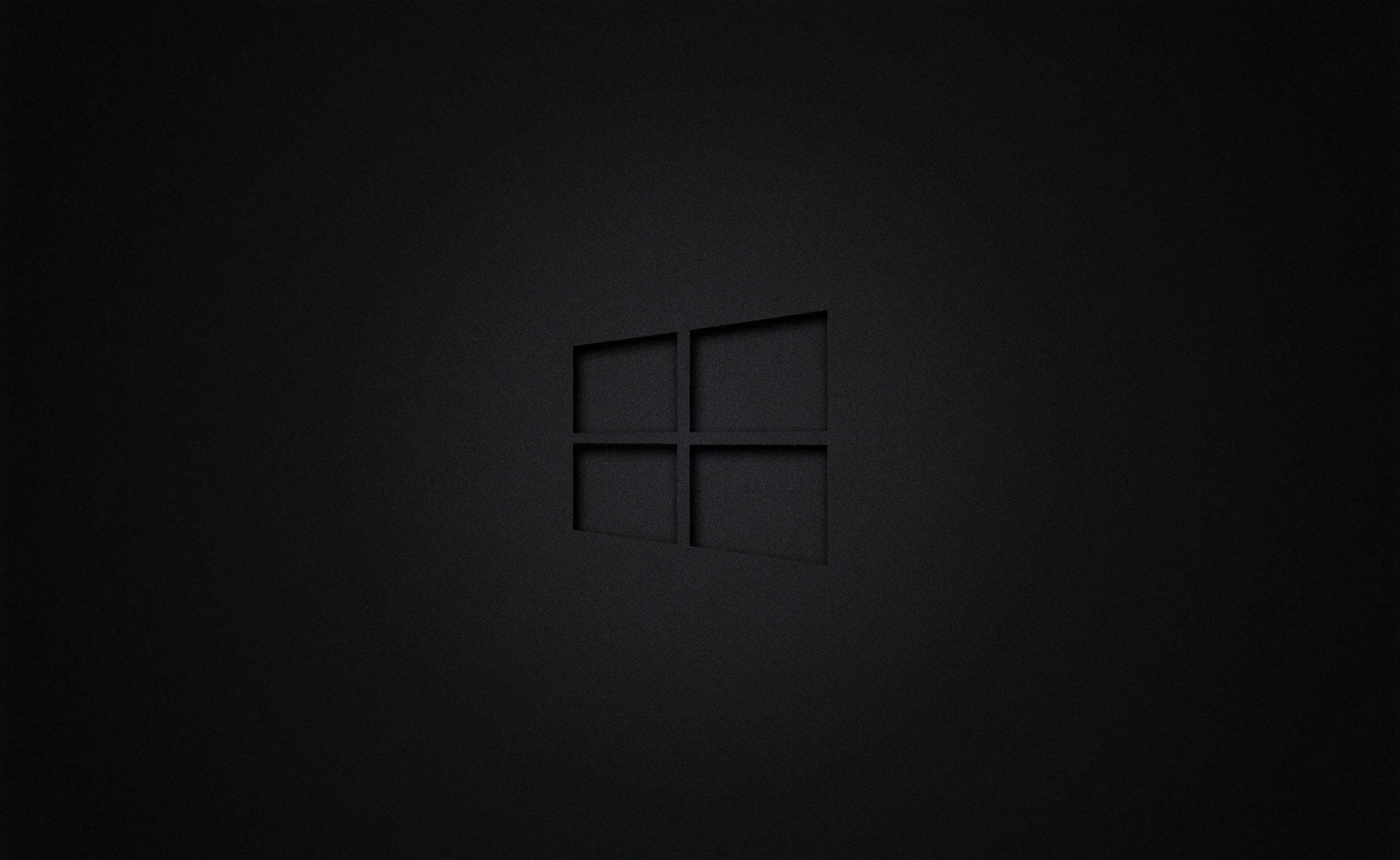 Logo 桌布 壁紙 — 一個極簡的黑色Windows標誌，在帶有柔和照明的紋理深色表面上微妙地壓印。