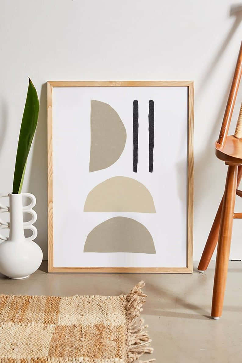 Modern Minimalist Art 桌布 壁紙 — 一個極簡風格的抽象藝術印刷品，帶有米色和黑色形狀，靠在一面白牆上，旁邊是一個帶有綠色葉子的白色花瓶和一把木椅。