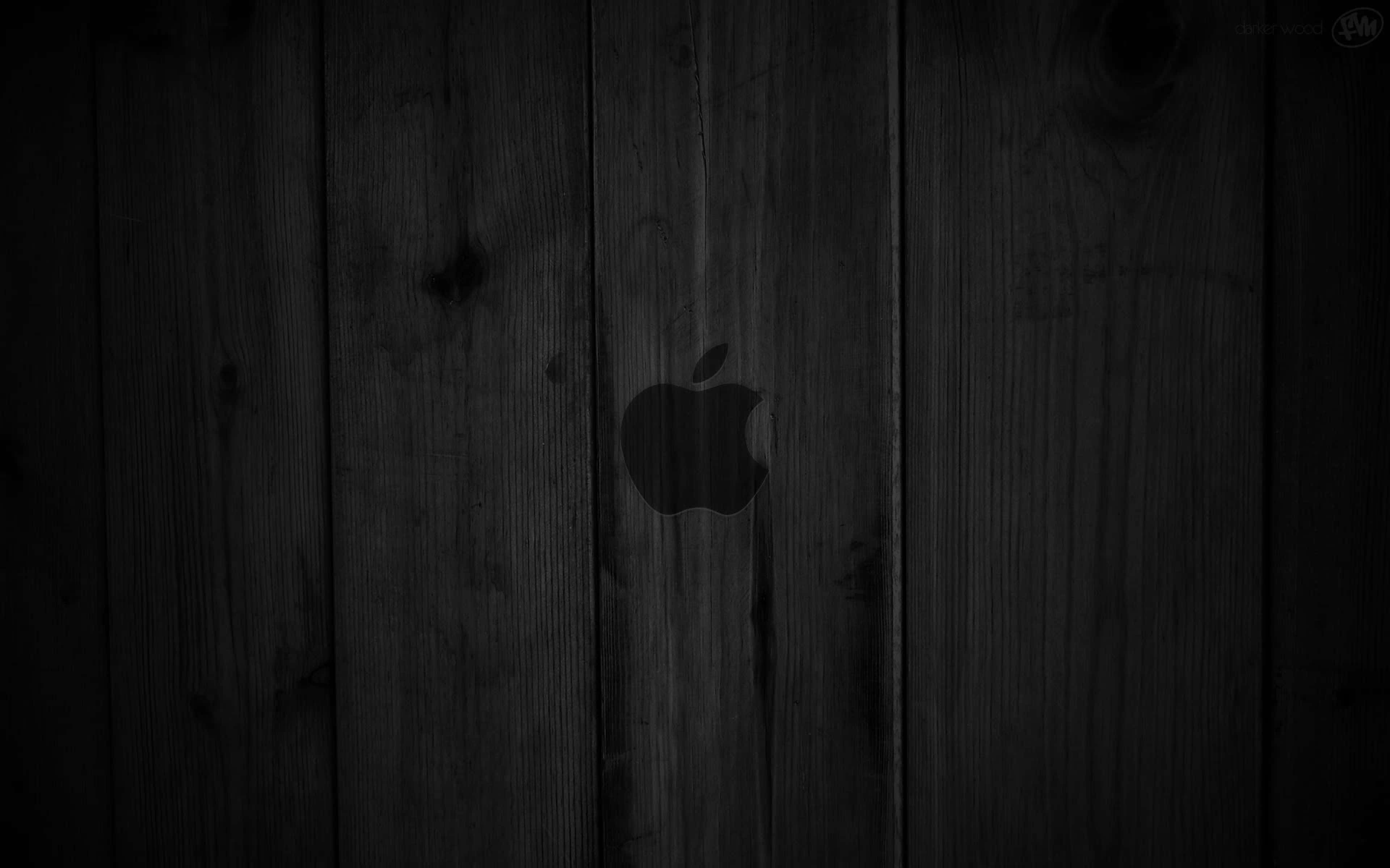 4K Apple 桌布 壁紙 — 一個極簡風格的黑色Apple標誌，微妙地置中於深色風化木板上，木紋與節疤清晰可見。