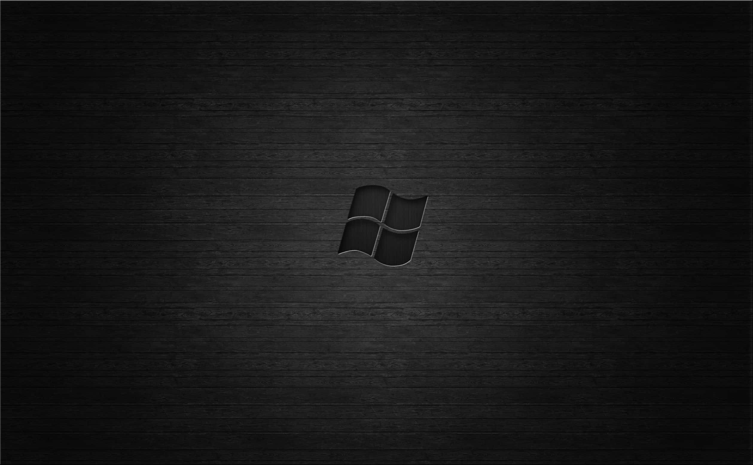 Minimalist Monochrome 桌布 壁紙 — 一個極簡黑色Windows標誌，置中於深色紋理木質表面上，帶有柔和燈光。