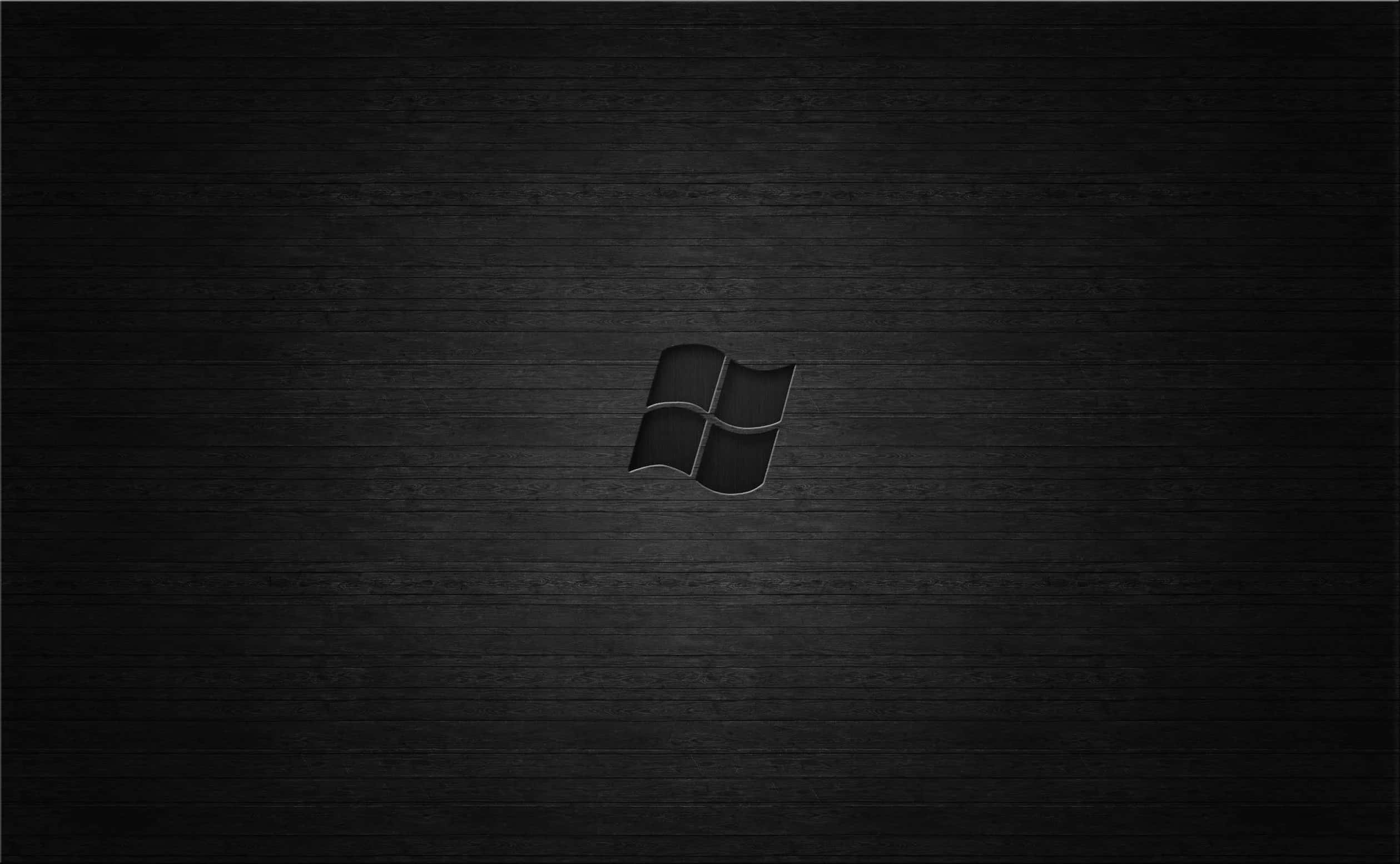 Black Windows 桌布 壁紙 — 一個極簡黑色Windows標誌，居中放置在深色紋理木質表面上，帶有柔和燈光。