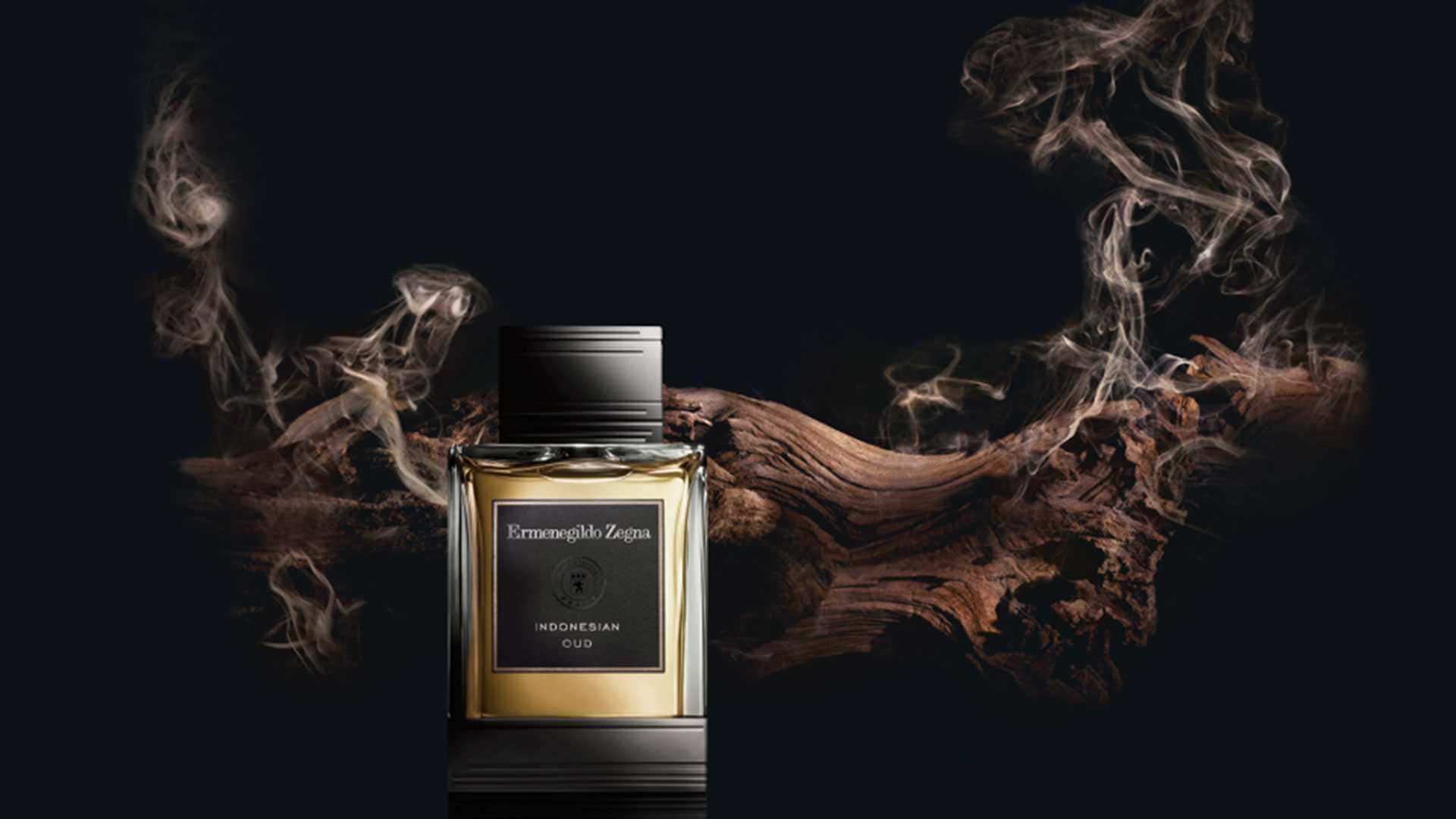 Fragrance 桌布 壁紙 — 一個標有Indonesian Oud的時尚金色香水瓶，在黑暗背景下，伴隨著旋轉的煙霧和紋理木材。
