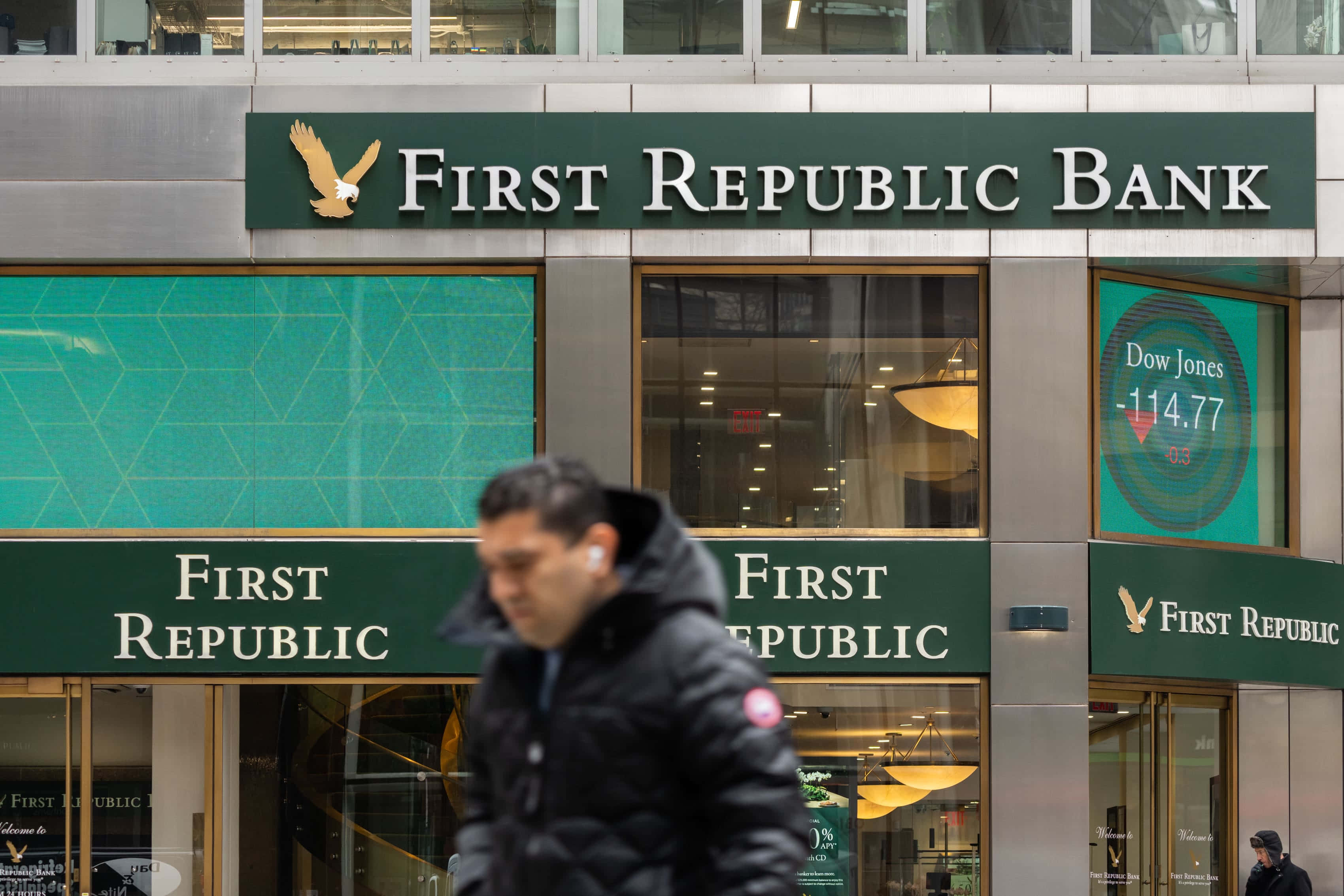 Bank 桌布 壁紙 — 一個模糊的行人走過第一共和銀行大樓，其數碼屏幕顯示道瓊斯指數下跌114.77點。