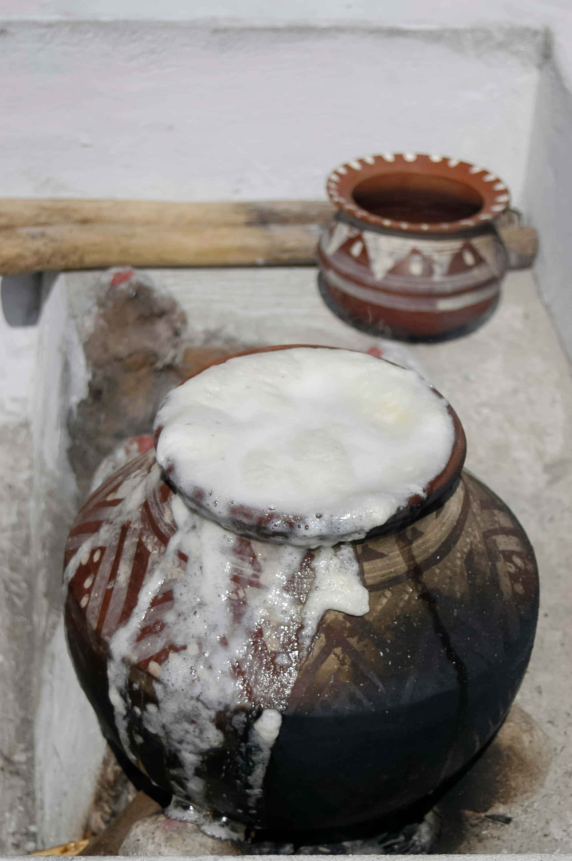 Pongal 桌布 壁紙 — 一個樸素的陶罐溢出白色泡沫，放在另一個裝飾罐旁邊，置於風化的石面上。