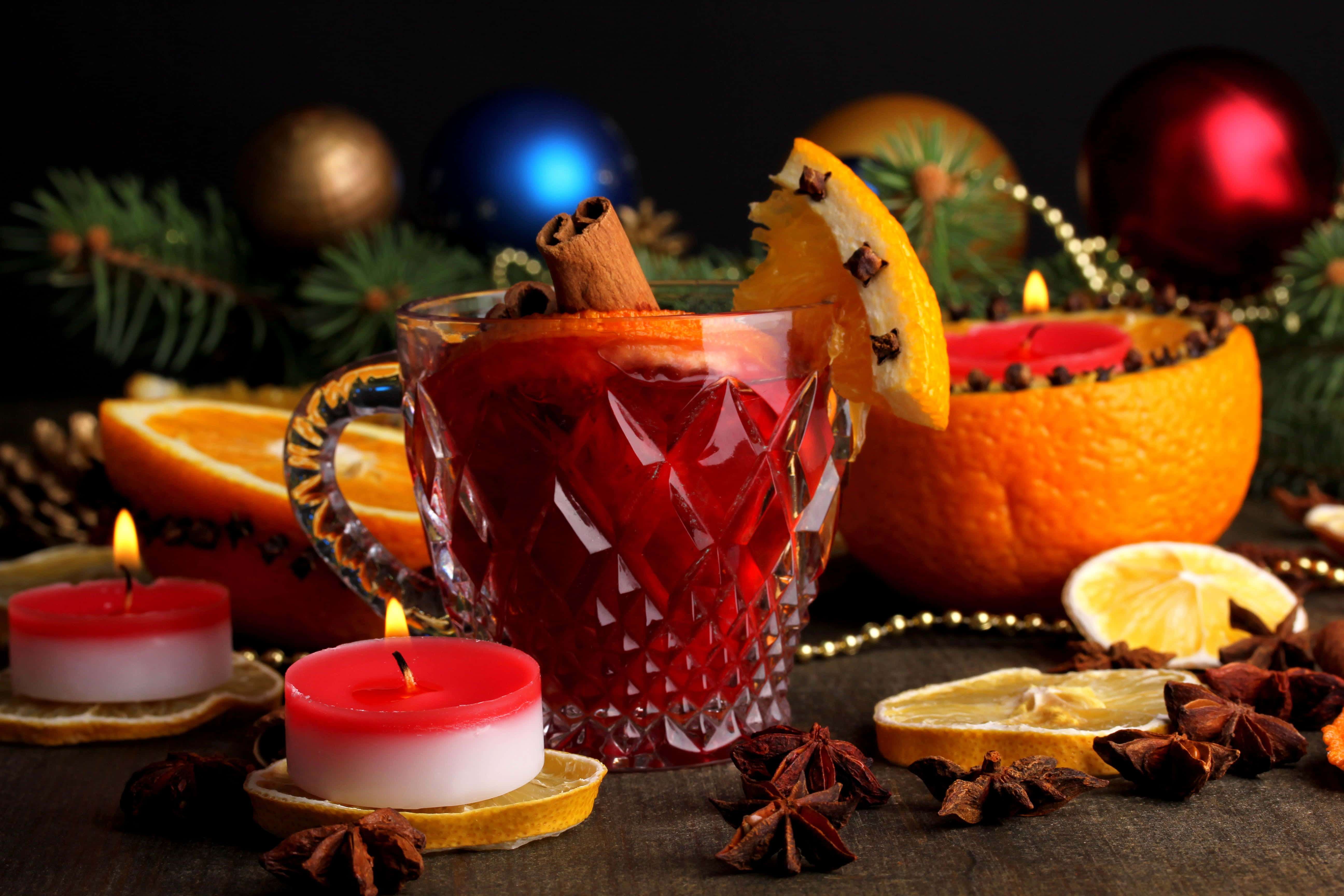 Mulled Wine 桌布 壁紙 — 一個水晶杯盛載著香料紅酒，飾以橙和肉桂棒，旁邊放著點燃的蠟燭和節日聖誕裝飾。