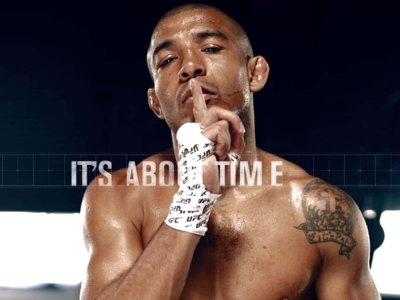 José Aldo：It's About Time 壁紙 — 一個汗流浹背、肌肉發達的戰士，手臂有紋身，在強光下將手指放在嘴唇上，專注集中。