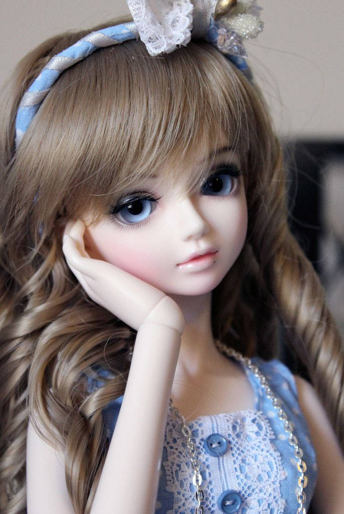 Doll 桌布 壁紙 — 一個洋娃娃的特寫，長長波浪形棕色頭髮和藍色眼睛，下巴擱在手上，穿著藍色蕾絲連衣裙和頭帶。