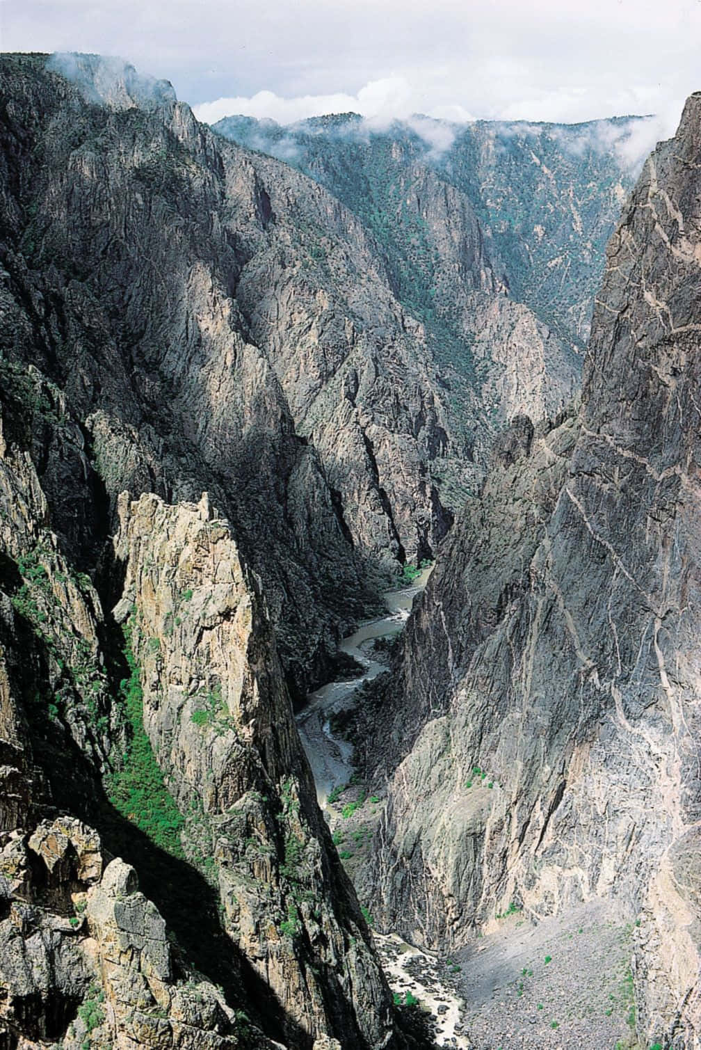 Black Canyon 桌布 壁紙 — 一個深峽谷，陡峭的岩石懸崖和下方蜿蜒的河流，天空多雲。