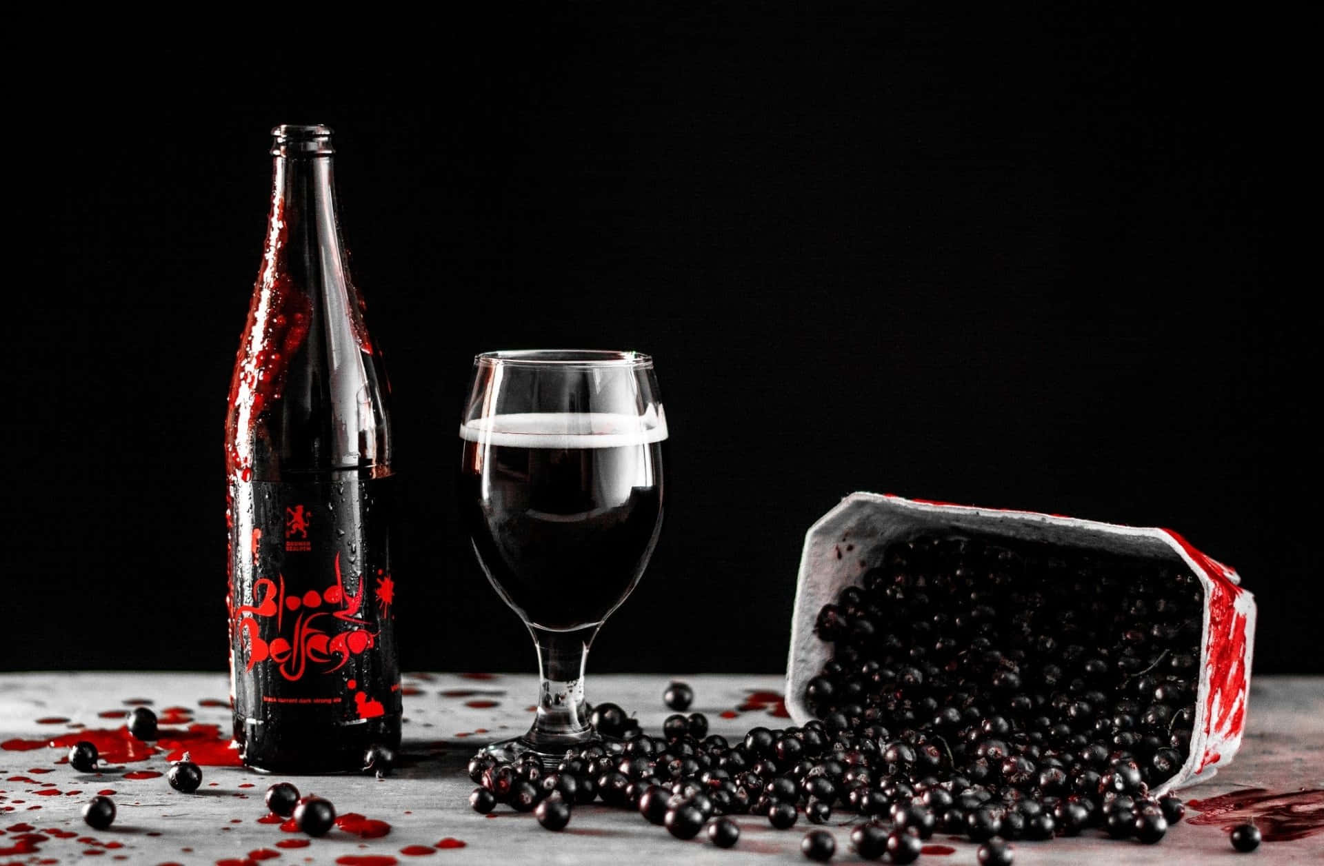 Black Wine 桌布 壁紙 — 一個深色啤酒瓶和玻璃杯放在灰色表面上，旁邊有灑落的黑加侖子和紅色液體，背景為黑色。