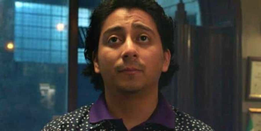 Flash Thompson 桌布 壁紙 — 一個深色捲髮、身穿波點恤衫的男人，在昏暗的房間裡向上望，露出驚訝的表情。