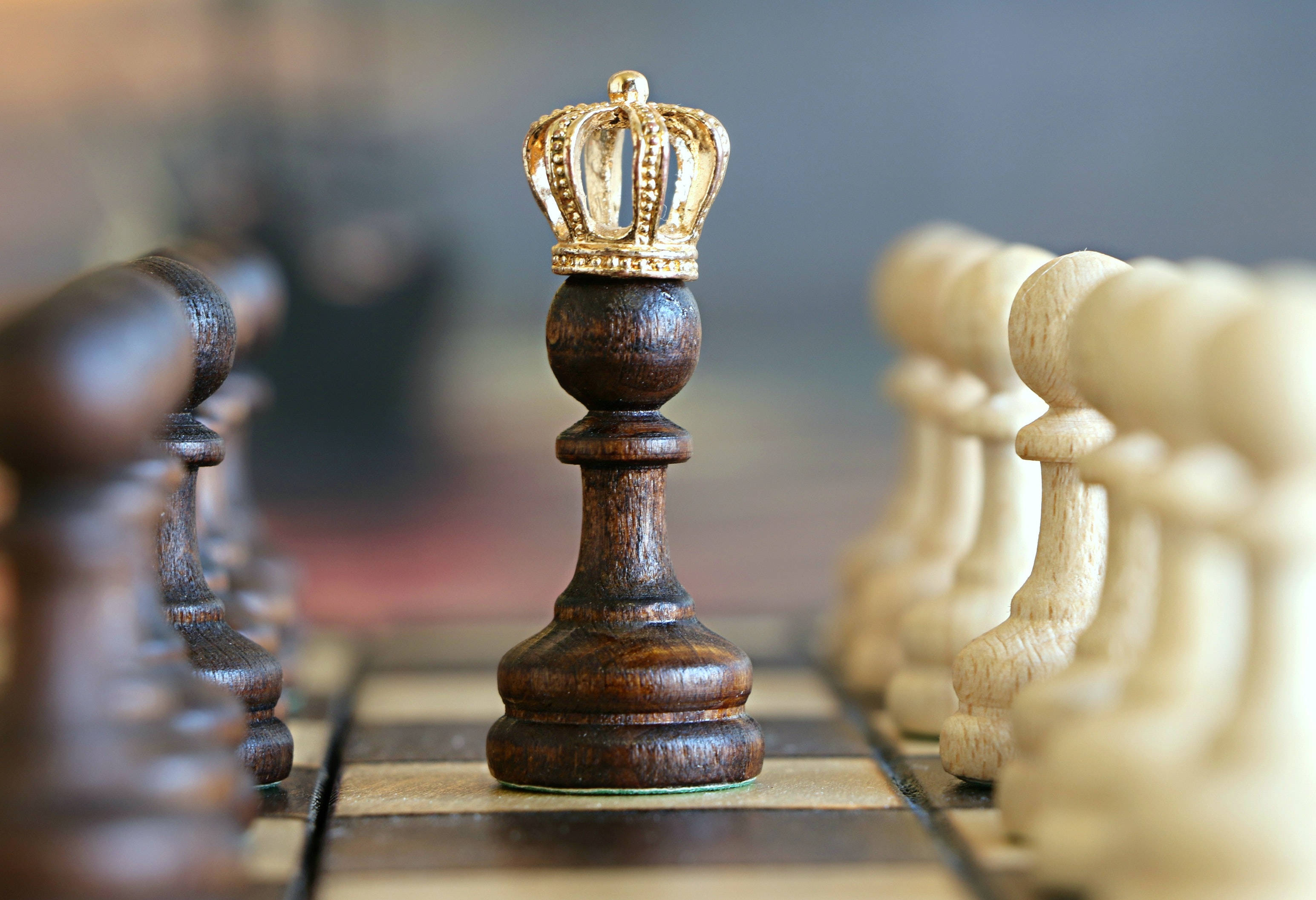 King And Queen 桌布 壁紙 — 一個深色木製國際象棋國王戴着金色王冠，站在棋盤上，面對白色棋子的特寫。