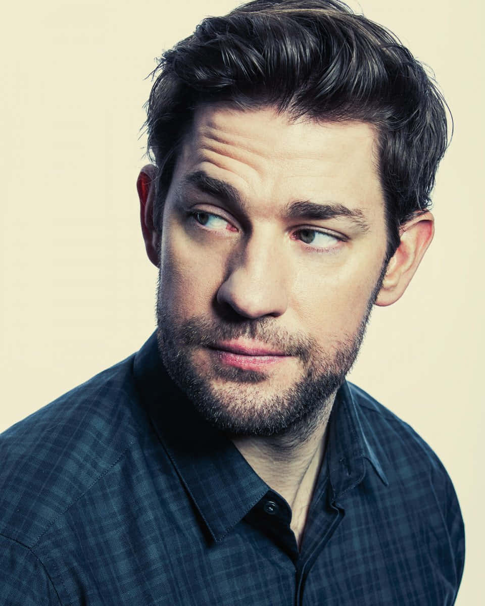 john krasinski 桌布 壁紙 — 一個深色頭髮、帶鬍渣的男人，在純米色背景下側目而視，表情若有所思。