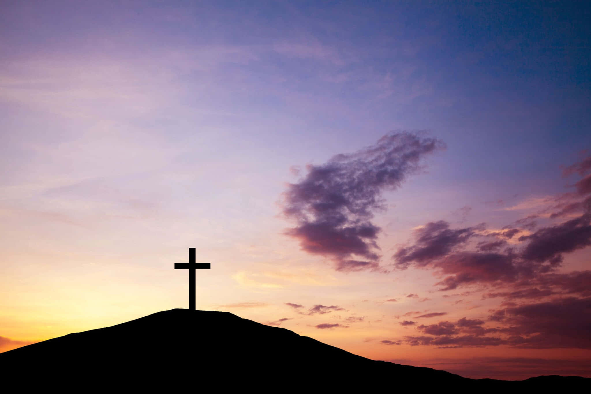 Good Friday 桌布 壁紙 — 一個清晰的十字架剪影矗立在山丘上，背景是充滿活力的暮色天空，點綴著紫色、橙色和粉紅色的雲彩。