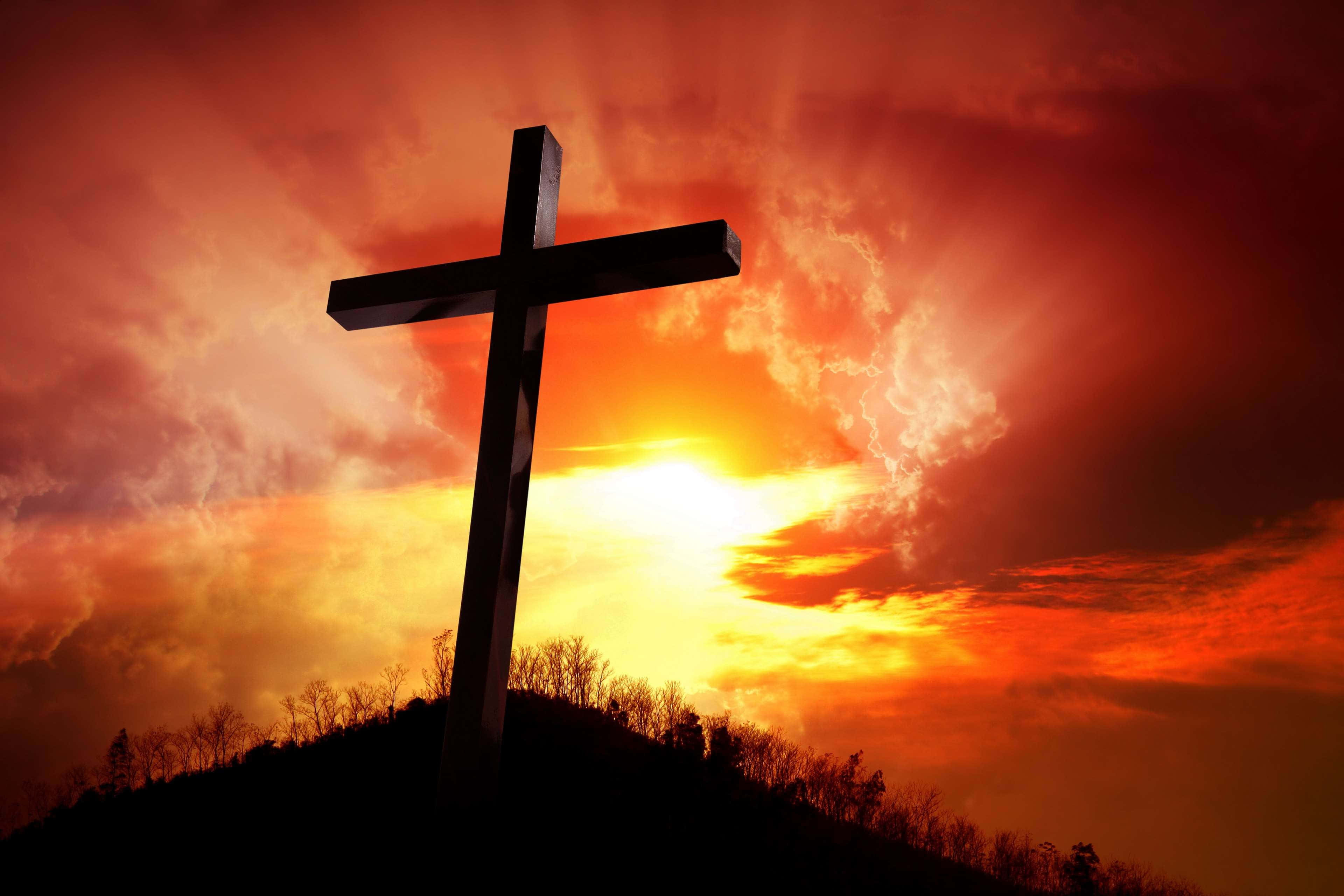 Jesus Resurrection 桌布 壁紙 — 一個清晰的十字架剪影矗立在山丘上，背景是熾熱的日落天空和光芒四射的雲彩。