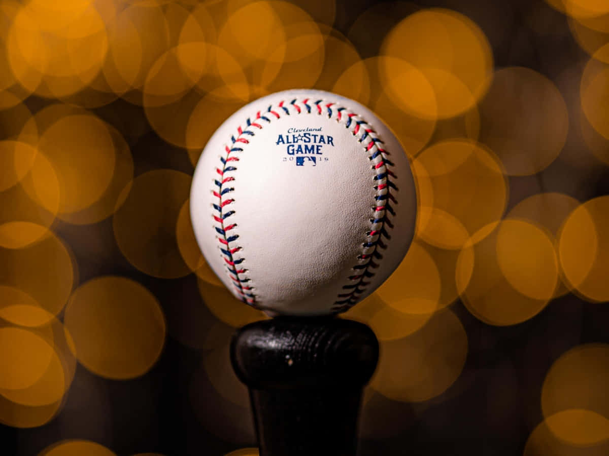 Cool Baseball 桌布 壁紙 — 一個清晰的棒球，帶有紅藍色縫線，放在球棒上，背景是溫暖的金色散景。