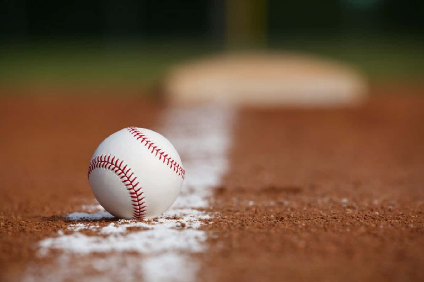 Cool Baseball 桌布 壁紙 — 一個清晰的棒球放在紅褐色泥土上，旁邊是粉筆畫的打擊區線，背景是本壘板模糊不清。