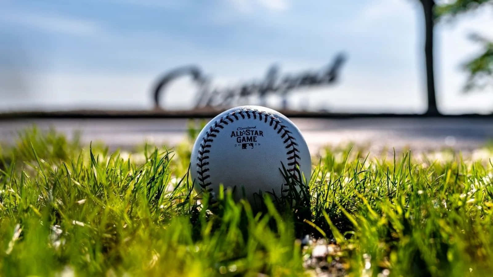 Cool Baseball 桌布 壁紙 — 一個清晰的棒球放在鮮綠色的草地上，背景有模糊的 'Cleveland' 標誌，天空明亮。