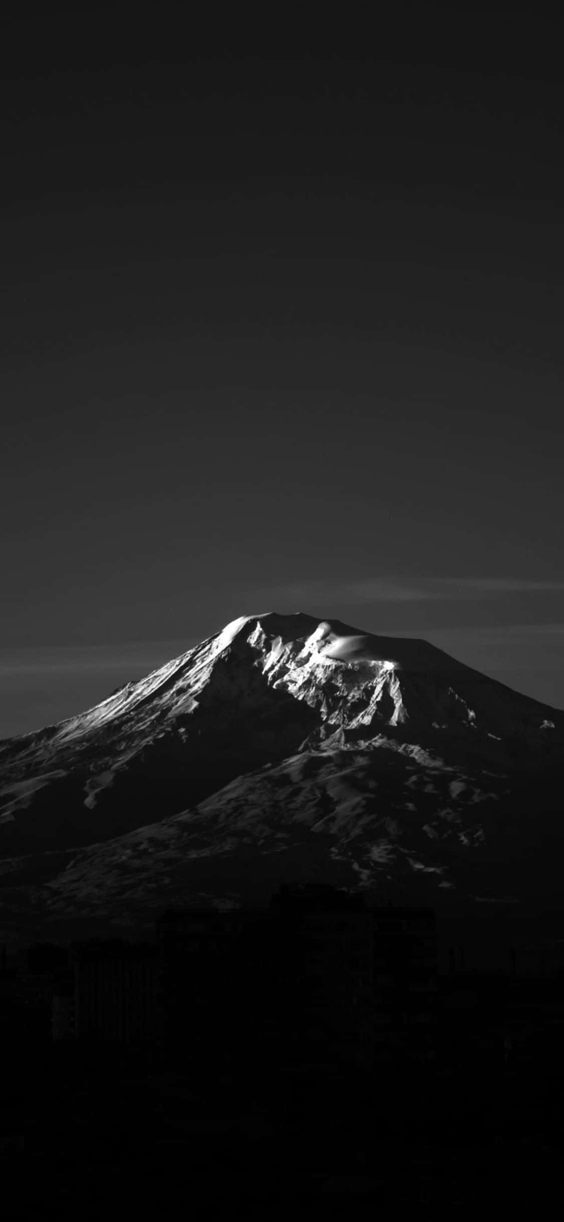 深色iPhone壁紙 桌布 壁紙 — 一個清晰的黑白山頂，積雪的山頂在黑暗的天空下，在剪影般的城市建築上方發光。