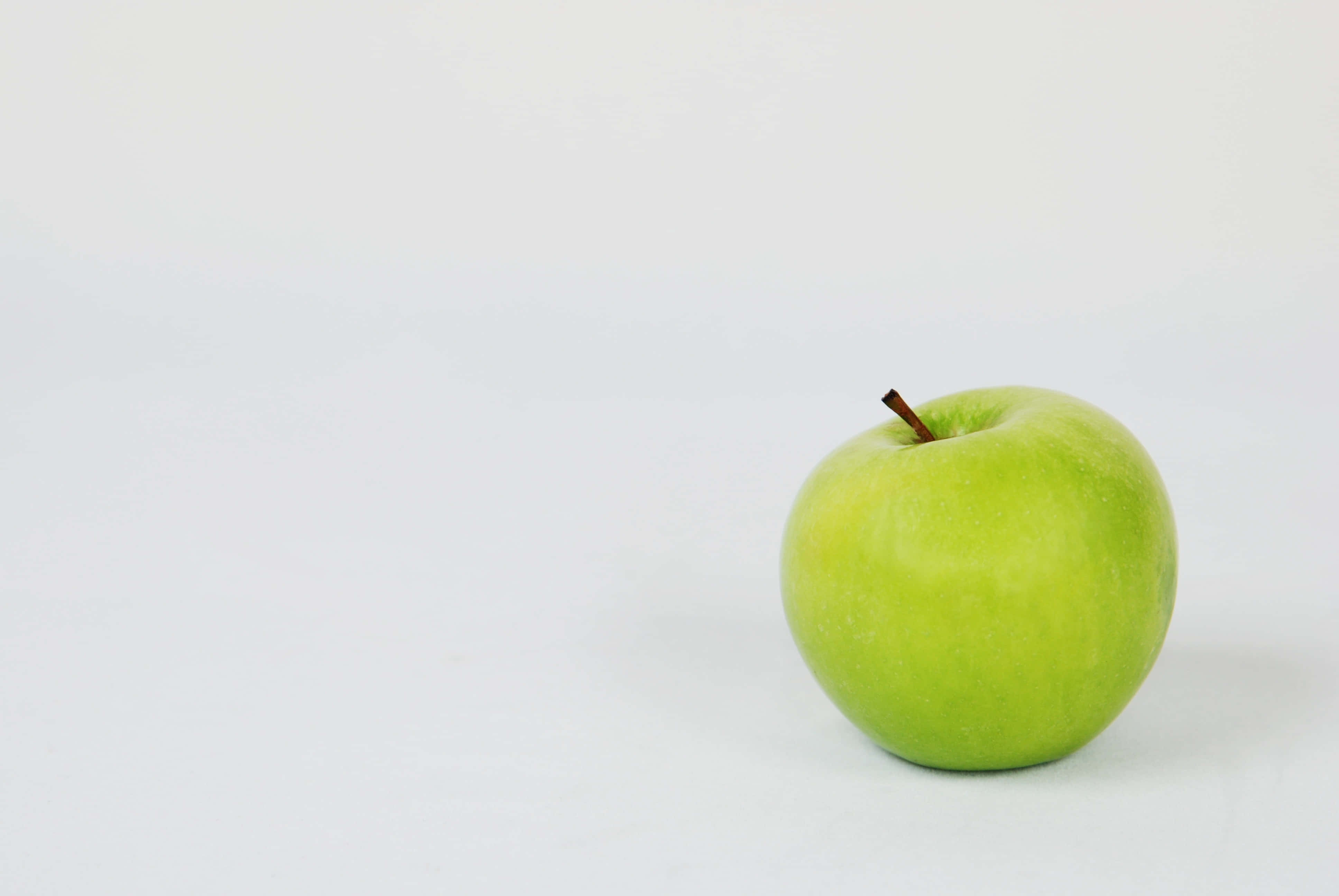 Summer Fruits 桌布 壁紙 — 一個清脆的青蘋果放在潔白的表面上，光線柔和均勻。