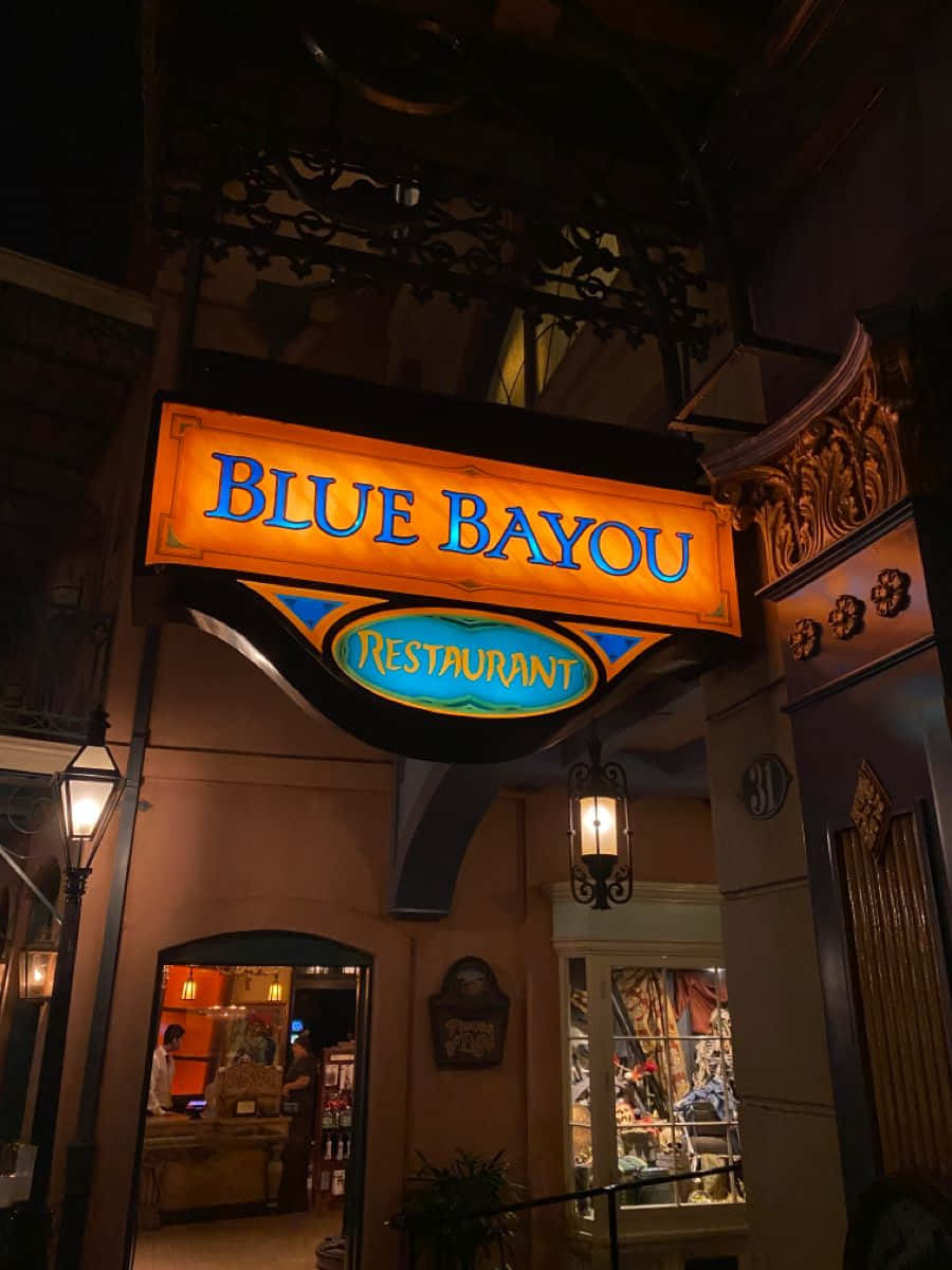 Blue Bayou 桌布 壁紙 — 一個溫暖照明的「Blue Bayou Restaurant」標誌在夜間於華麗入口上方發出橙色和藍色的光芒。