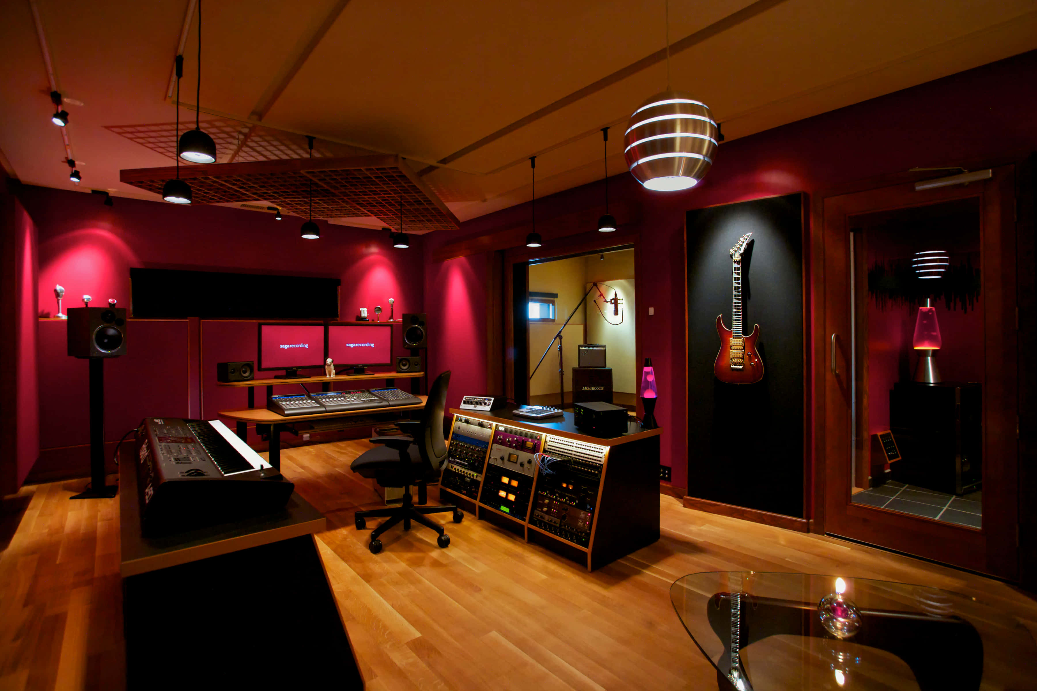 Studio 桌布 壁紙 — 一個溫暖照明的專業音樂工作室，配有紅色牆壁、木地板和環境燈光下的音響設備。