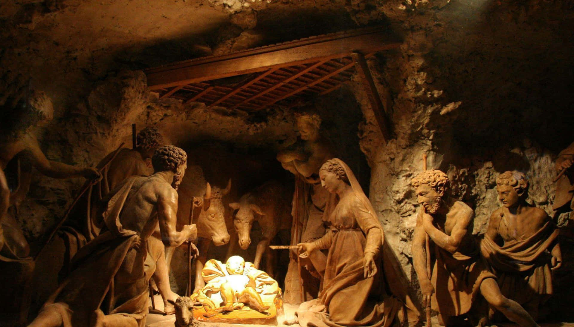 Nativity 桌布 壁紙 — 一個溫暖照明的耶穌誕生場景，有詳細的瑪利亞、約瑟和牧羊人雕像，聚集在岩石洞穴中的嬰兒耶穌周圍。