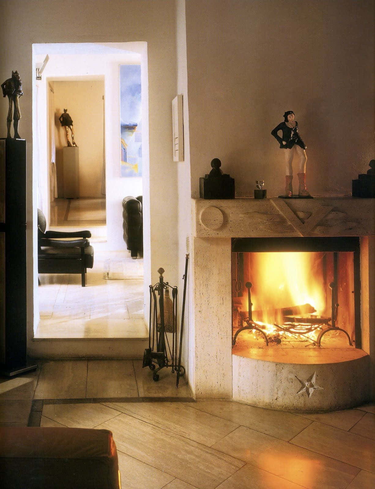 Cozy Fire 桌布 壁紙 — 一個溫暖發光的壁爐，位於簡約風格的室內，配有石磚和壁爐架上的雕像，投射出柔和的光線。