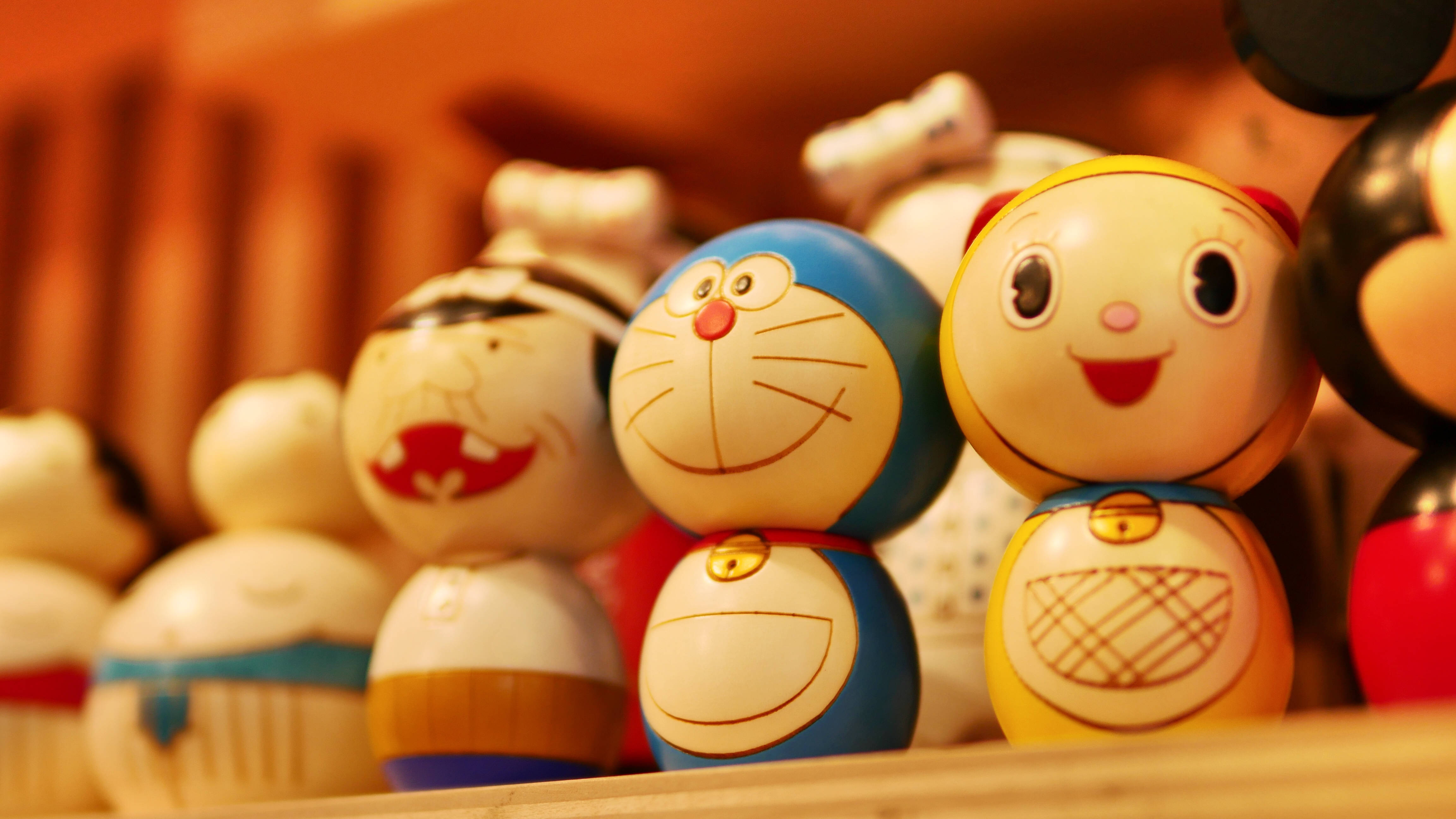 Doraemon 桌布 壁紙 — 一個溫暖的特寫鏡頭，展示色彩繽紛的日本木芥子娃娃，帶有歡樂的卡通面孔，排列在木架上。