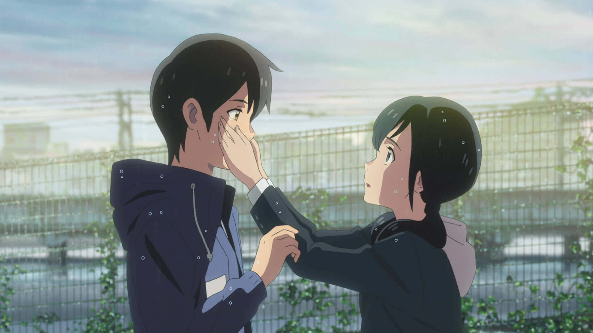 Weathering With You 桌布 壁紙 — 一個溫柔的動漫時刻，女孩輕輕觸摸男孩的臉龐，雨滴在他們周圍落下，處於柔和的都市環境中。