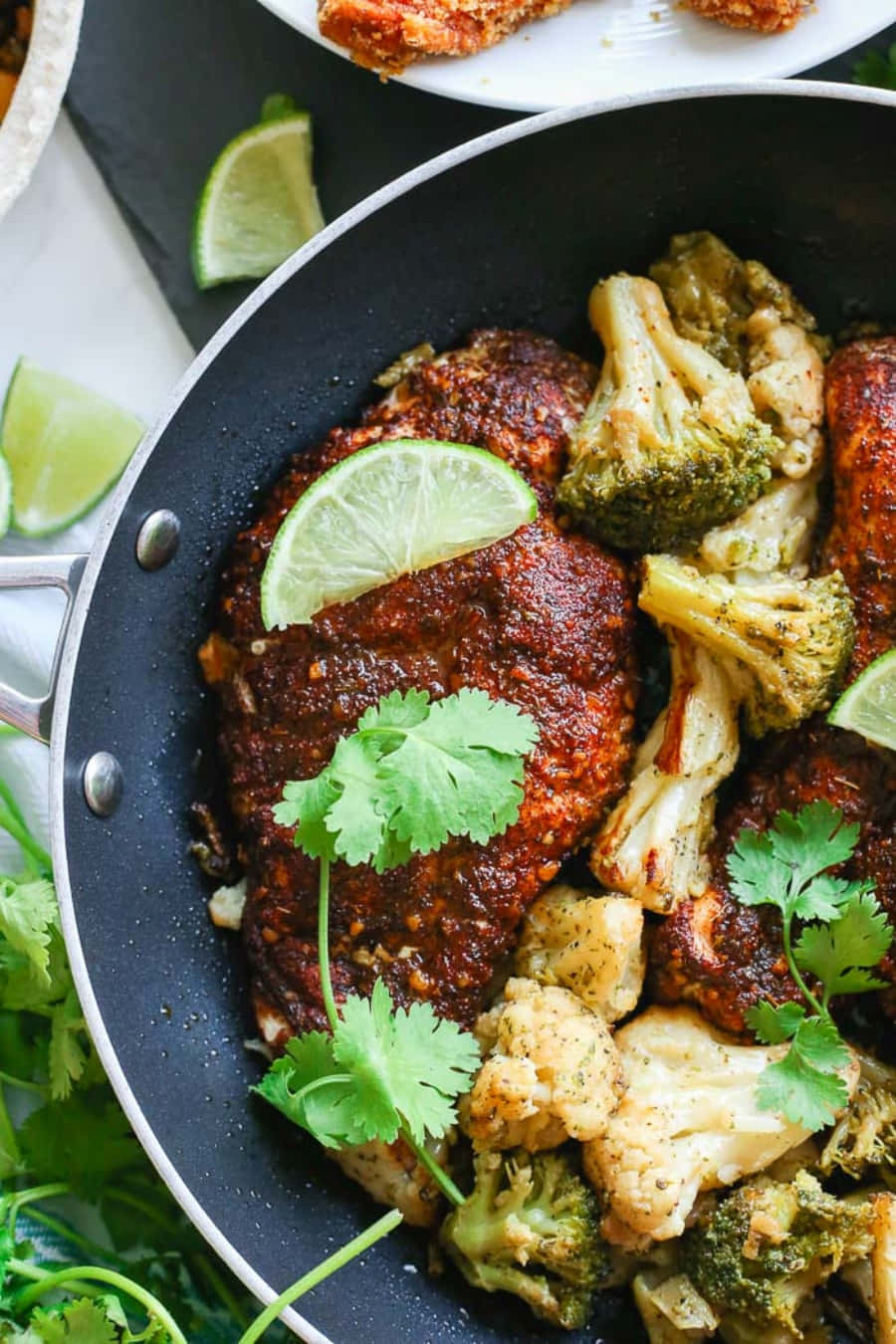 Blackened Chicken 桌布 壁紙 — 一個滋滋作響的煎鍋裡有香料邊雞肉和烤西蘭花，上面放上新鮮芫荽和青檸角。