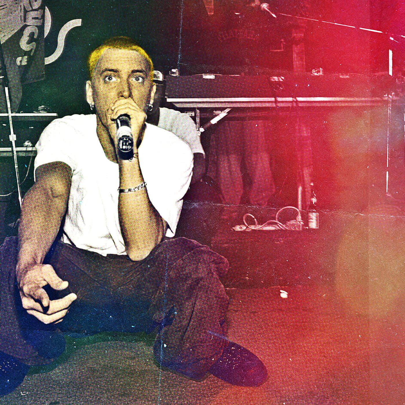 Eminem 桌布 壁紙 — 一個漂染金髮的年輕男子坐在舞台上，在紅色和綠色的舞台燈光下拿著咪高峰。