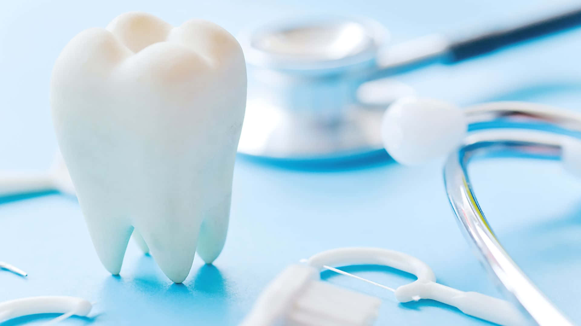 Tooth 桌布 壁紙 — 一個潔白的牙齒模型與聽診器和牙科工具一起清晰地聚焦在清涼的藍色表面上。