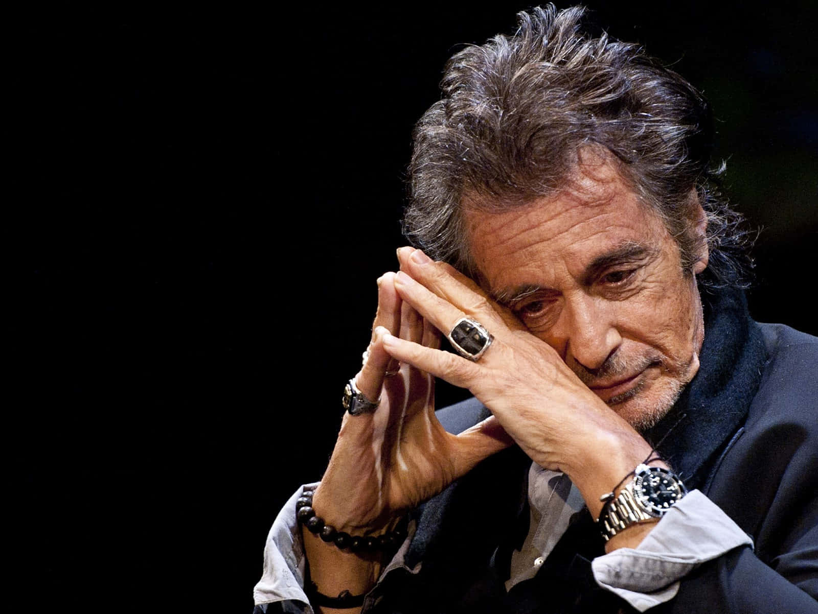 Al Pacino 桌布 壁紙 — 一個灰白頭髮、眼神銳利的男人特寫，雙手在黑色背景前交握於臉旁。