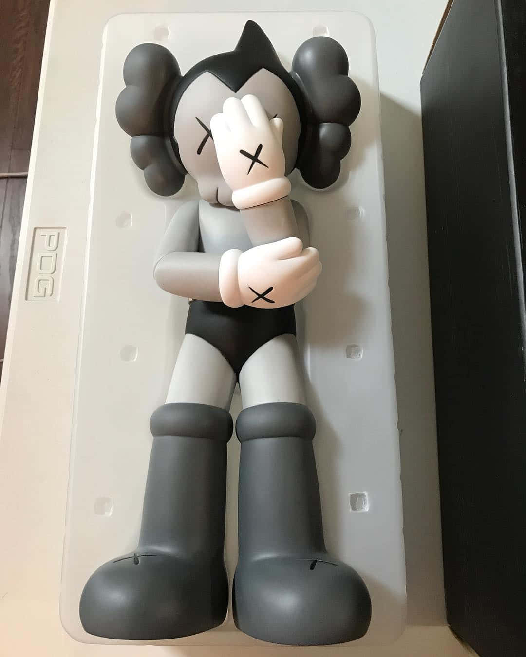 Kaws Astro Boy 桌布 壁紙 — 一個灰色和白色的KAWS人偶，帶有X形眼睛和雲朵般的頭髮，躺在白色泡沫包裝托盤中。