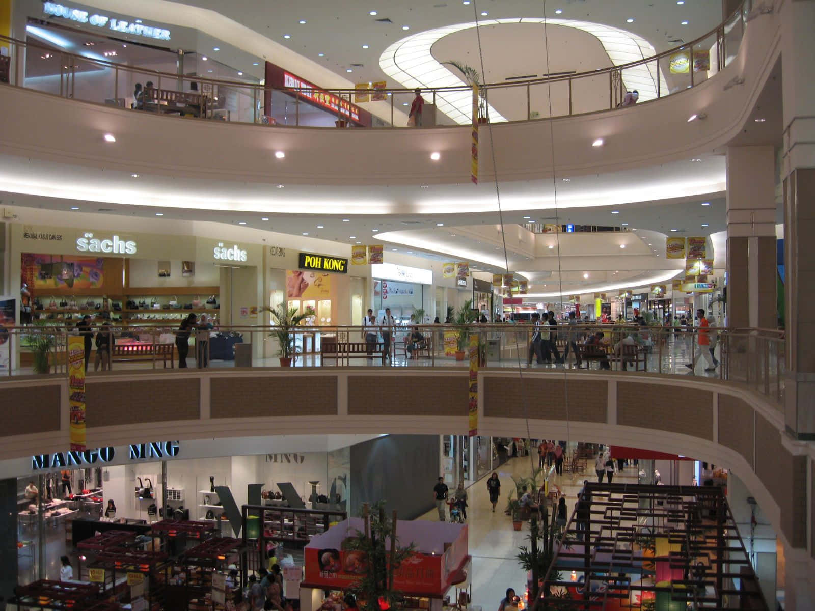 Mall 桌布 壁紙 — 一個熙熙攘攘的多層購物中心，設有弧形走道、購物者和明亮的商店招牌，在人工照明下。