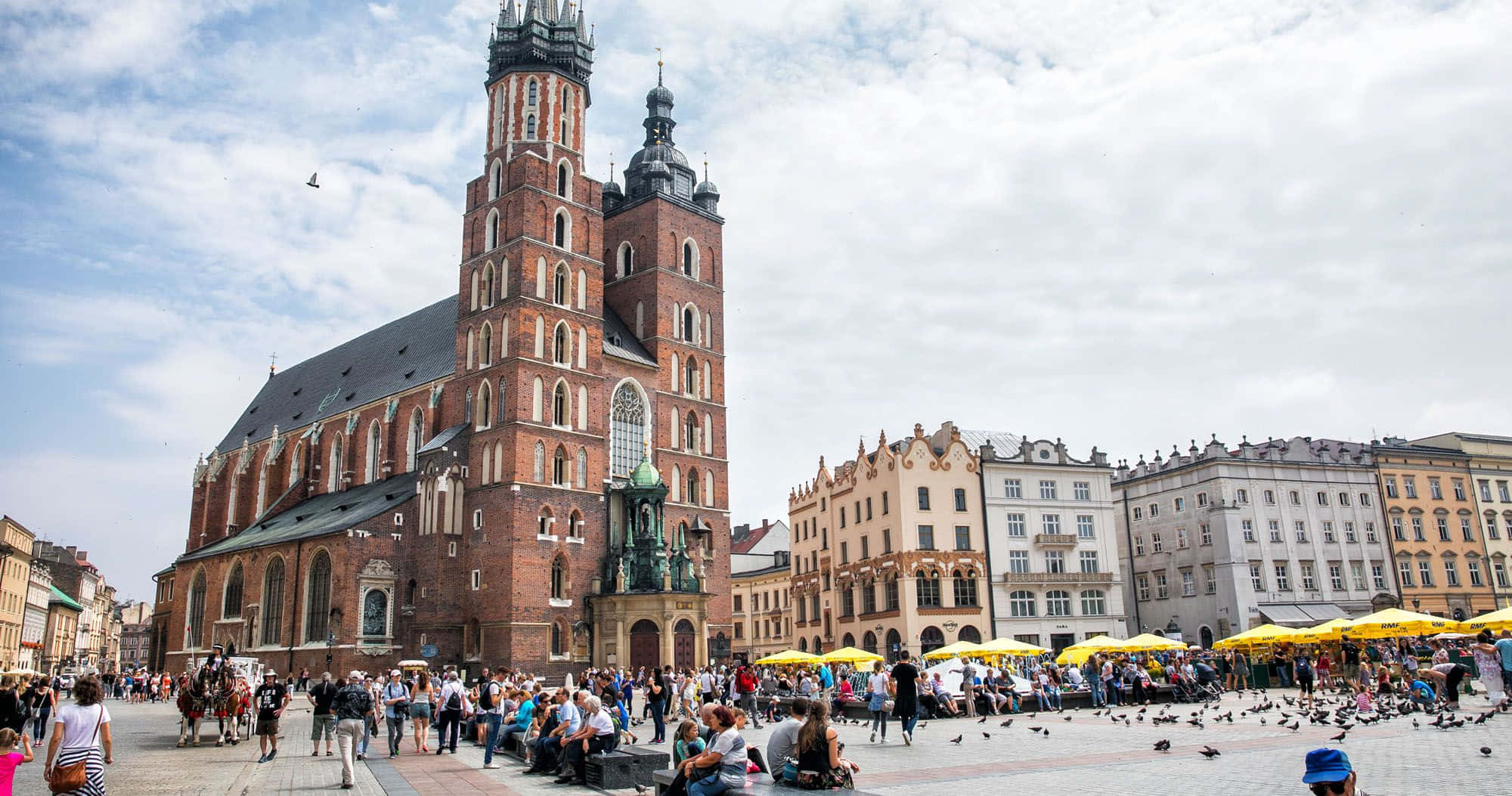 Poland 桌布 壁紙 — 一個熱鬧的歐洲廣場，有一座高聳的紅磚哥德式教堂，人們在陰天享受黃色雨傘。