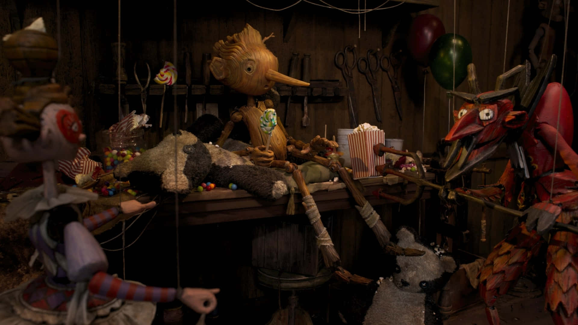 Guillermo Del Toro's Pinocchio 桌布 壁紙 — 一個燈光昏暗的木偶劇院，充滿了木製牽線木偶和散落的糖果，在一個雜亂的工作室裡。