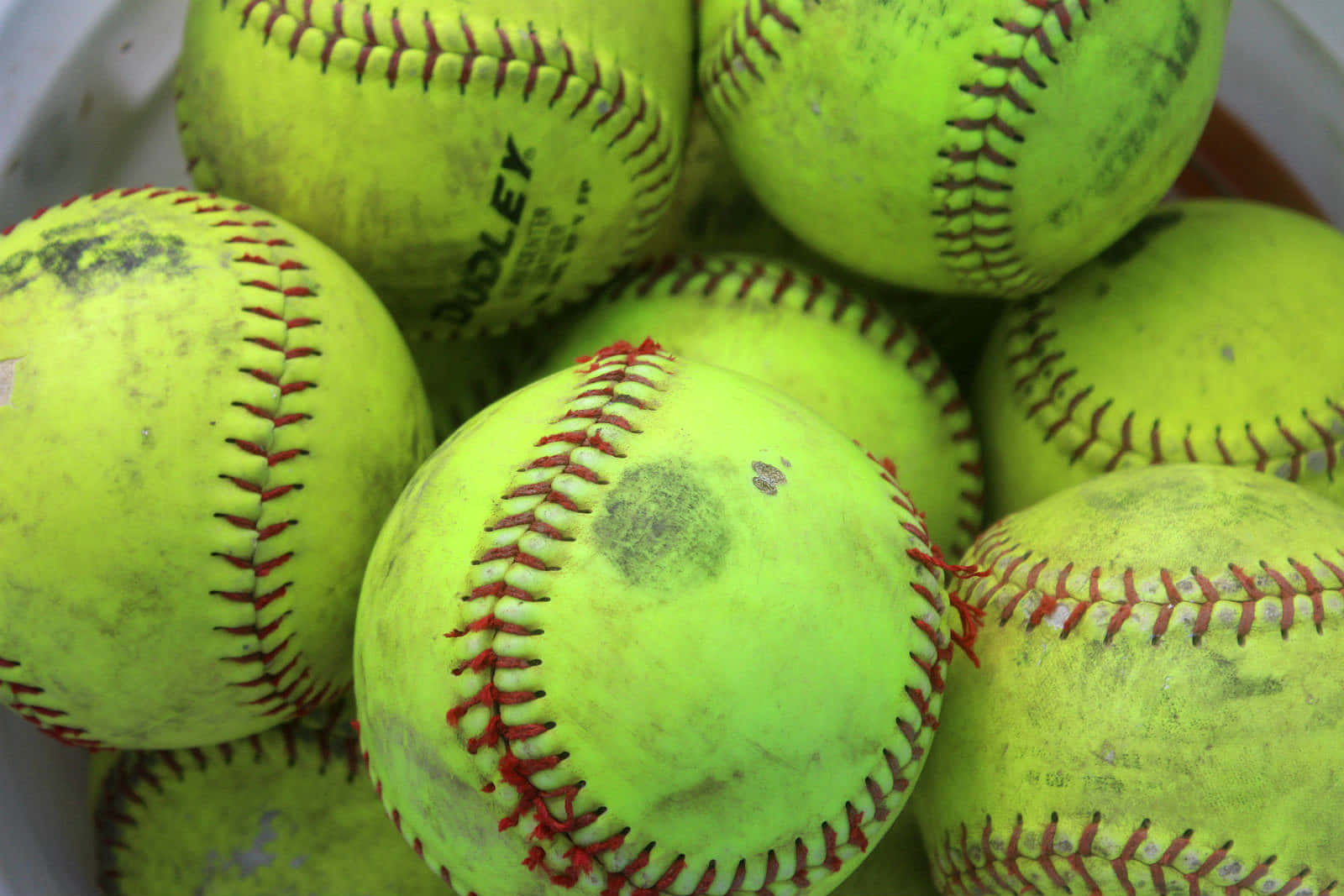 Softball 桌布 壁紙 — 一個特寫，展示磨損的螢光黃色壘球，帶有紅色縫線，堆疊在一個容器中。